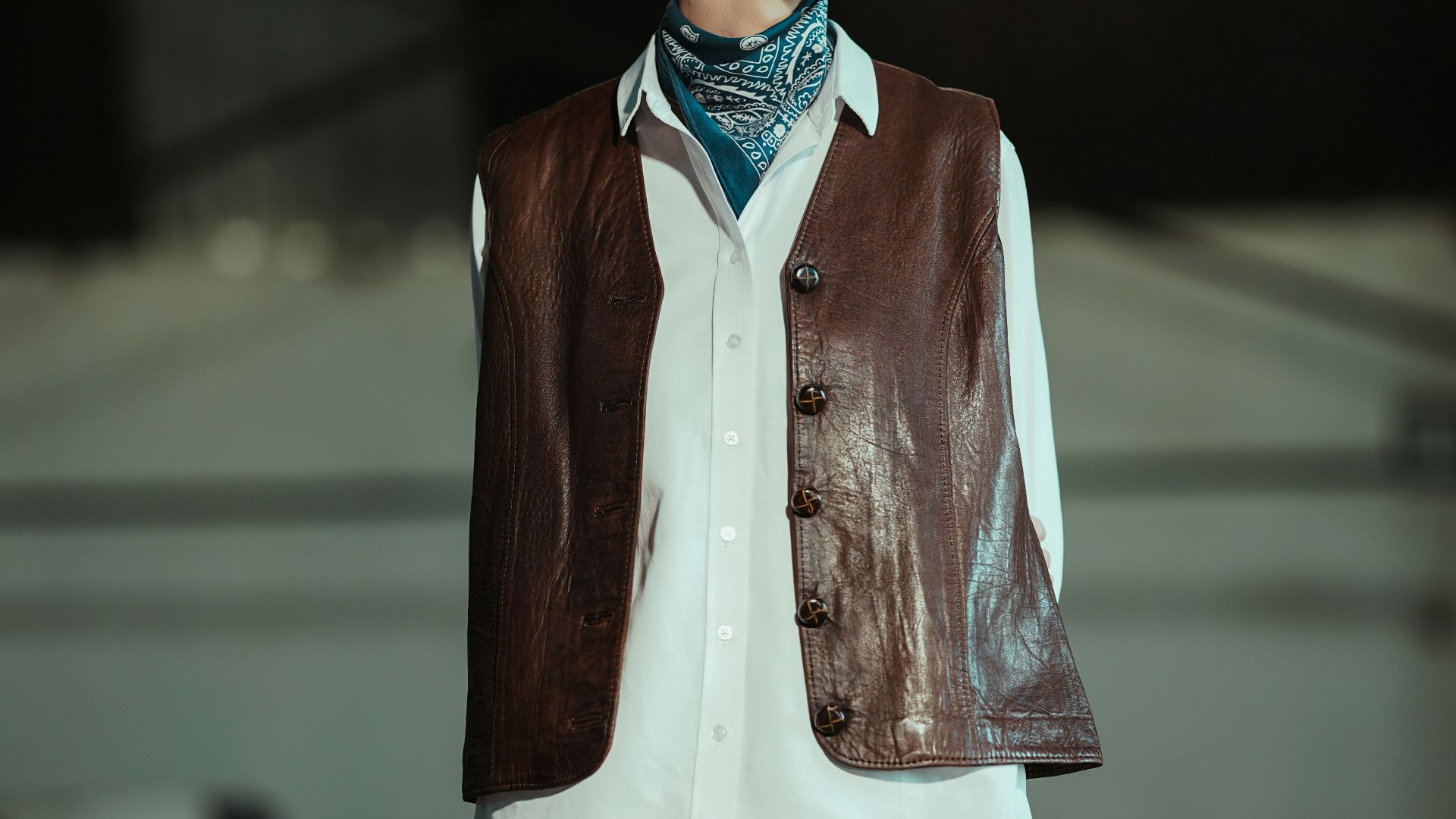 Young person in a vest and bandana looks away.