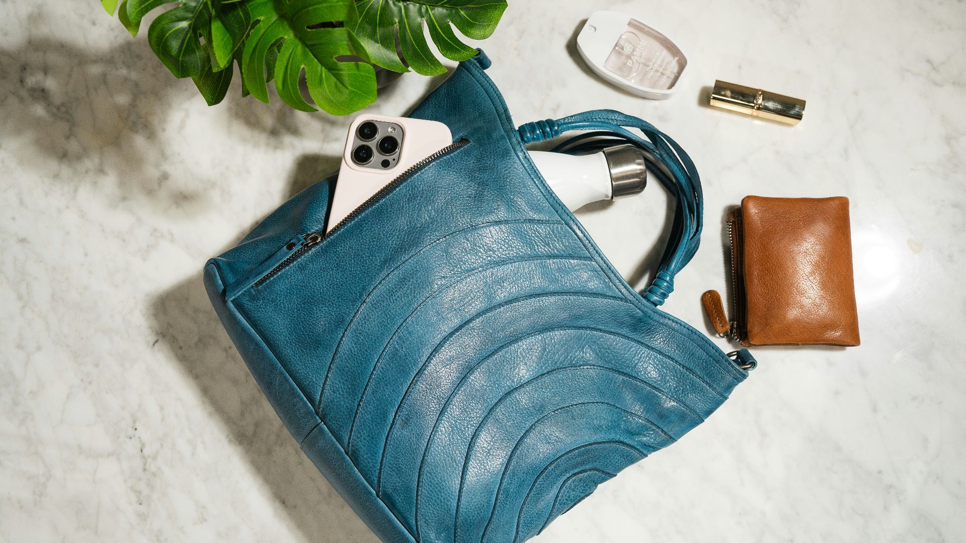 Teal leather handbag with phone, wallet, and makeup.