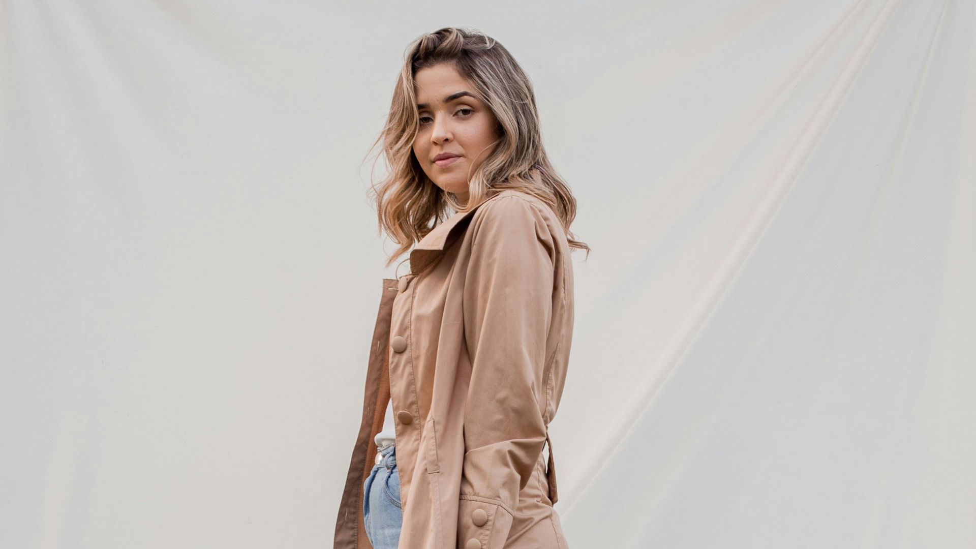woman in brown coat and blue denim jeans standing on white textile