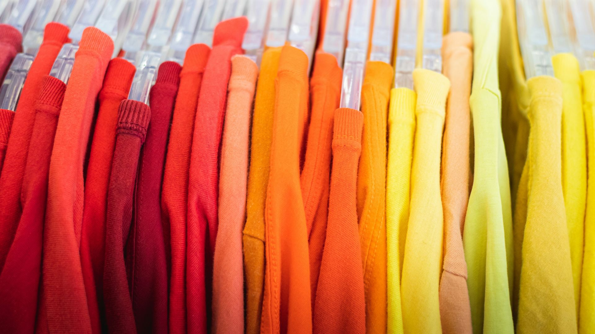 a bunch of different colored shirts hanging on a rack