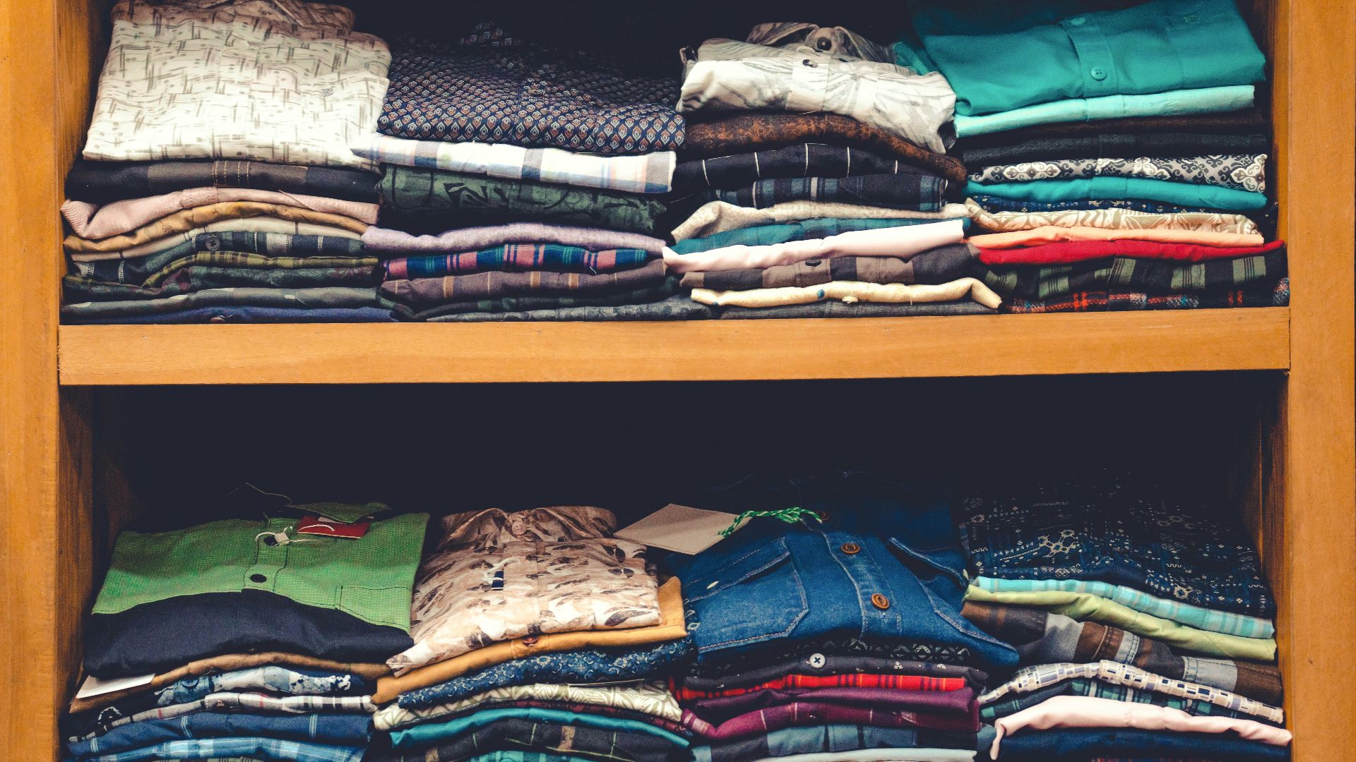 a wooden shelf filled with lots of folded shirts