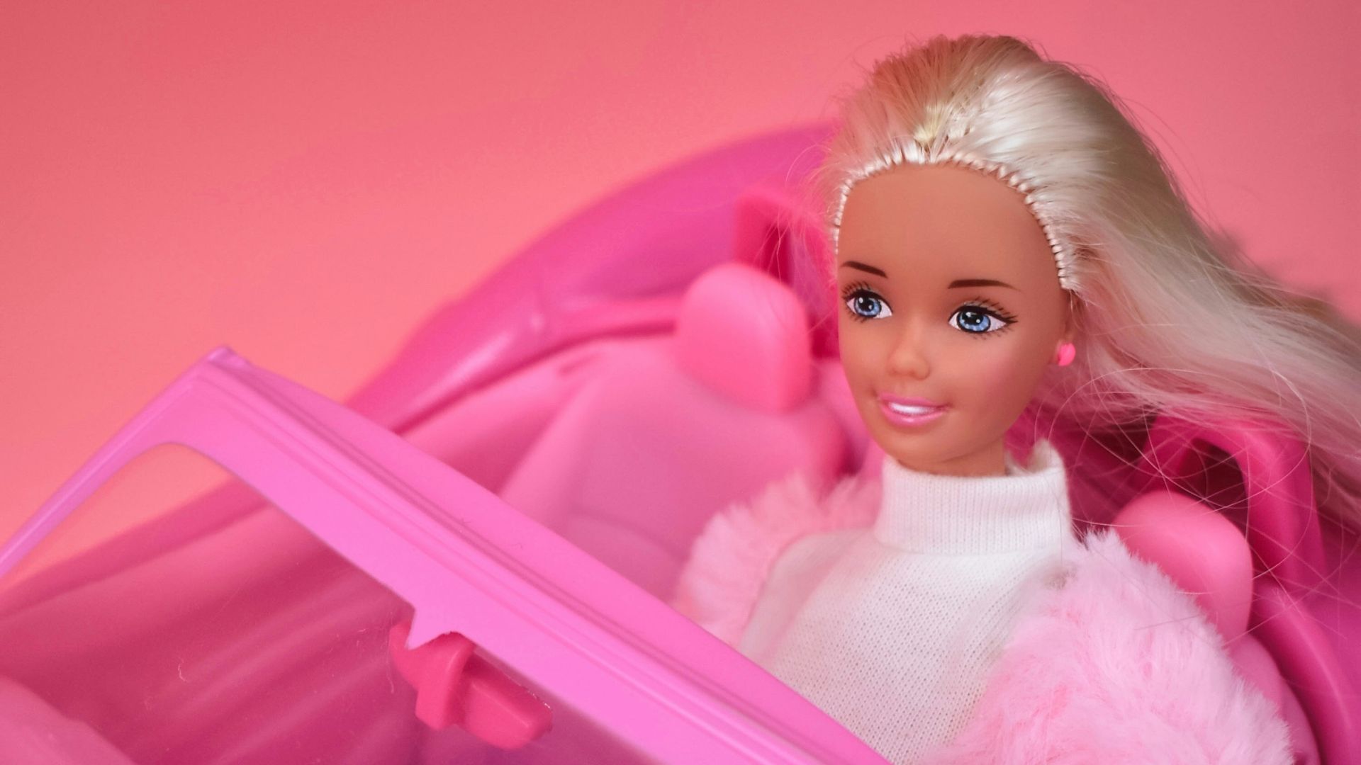 A barbie doll sitting in a pink car