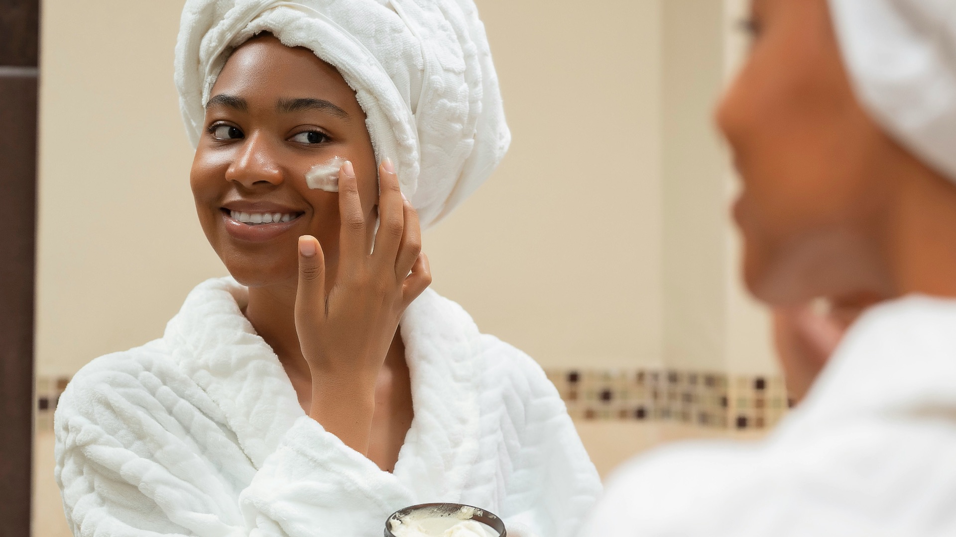 a woman with a towel on her head and a jar of cream on her face