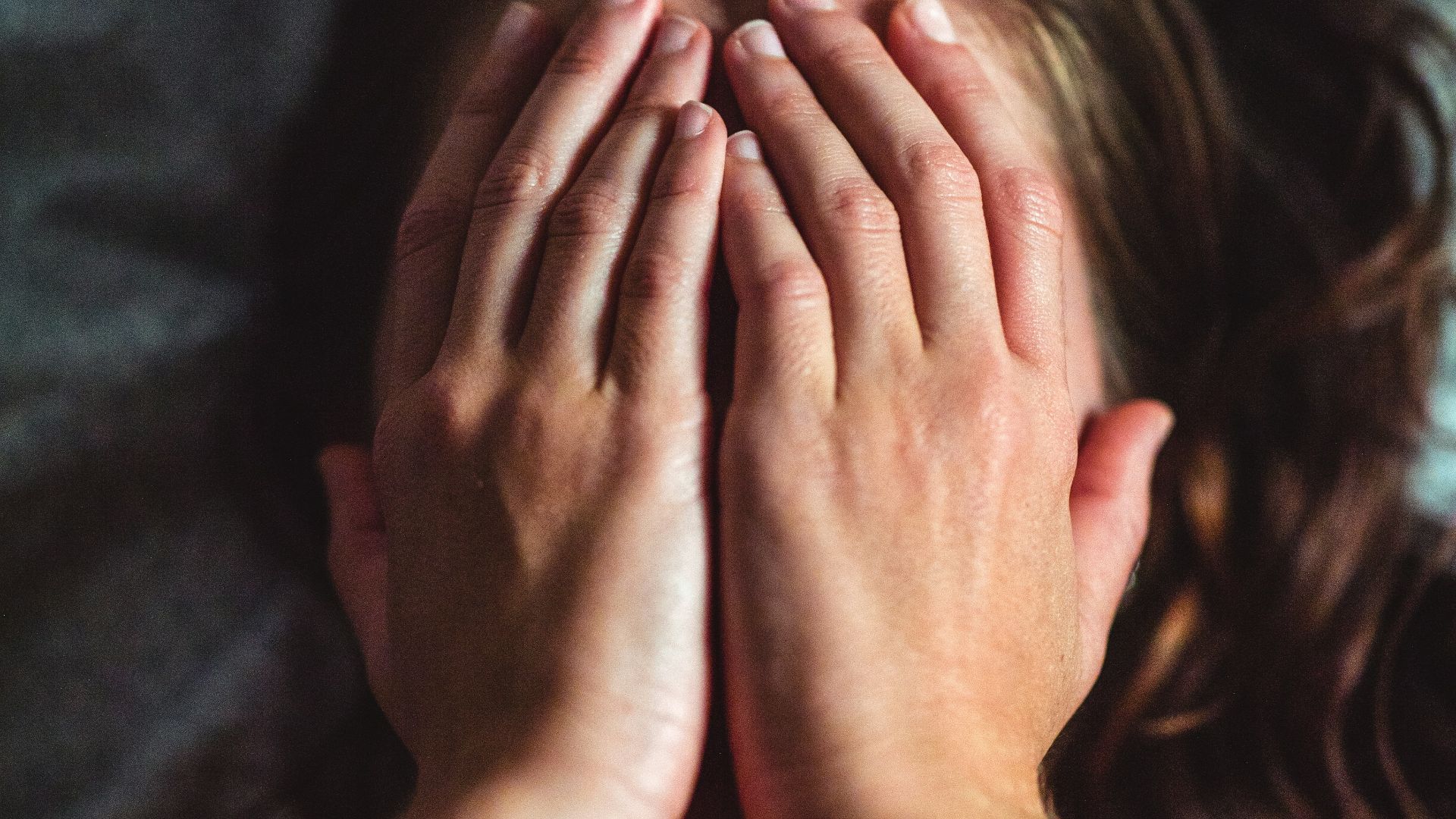 woman covering face lying on gray bed