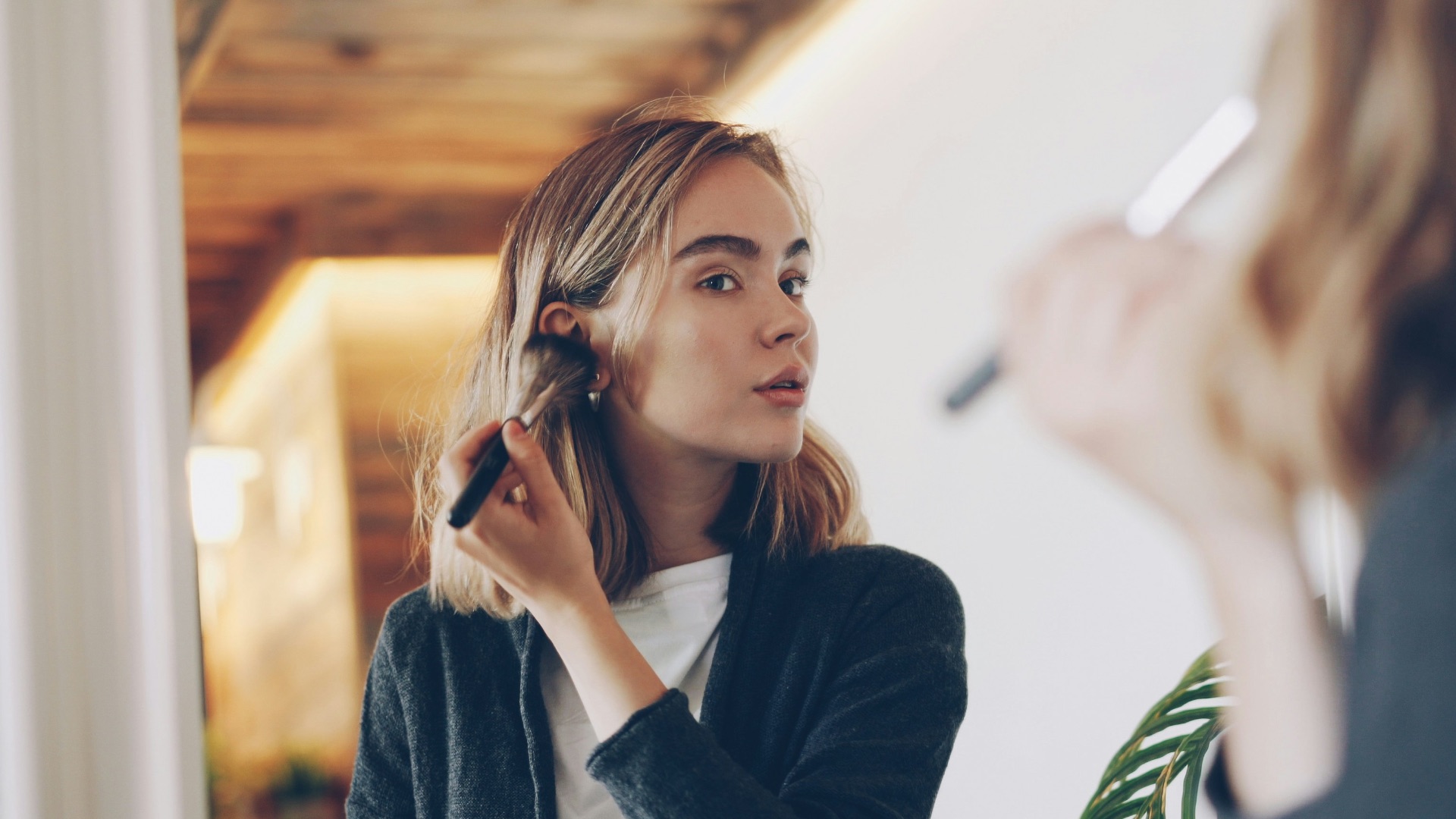 Young woman applying makeup in mirror.