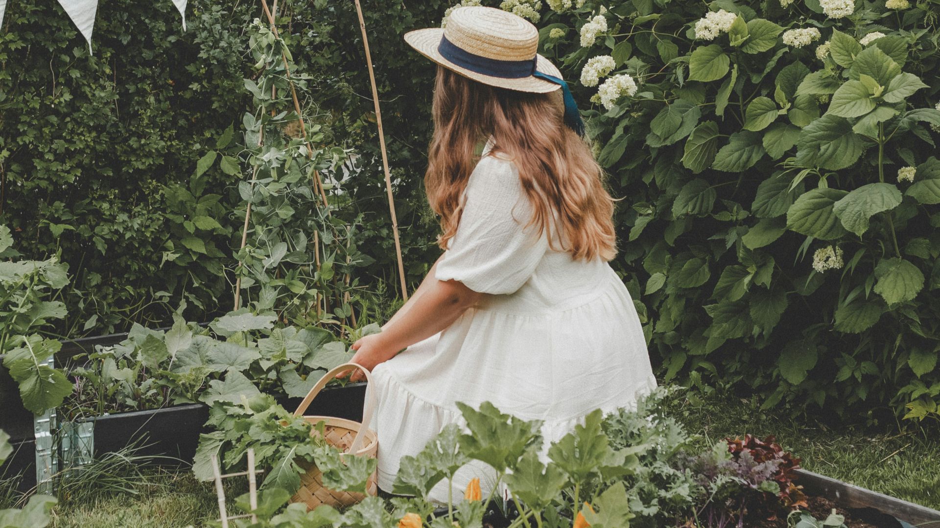 a woman in a white dress and hat tending to a garden