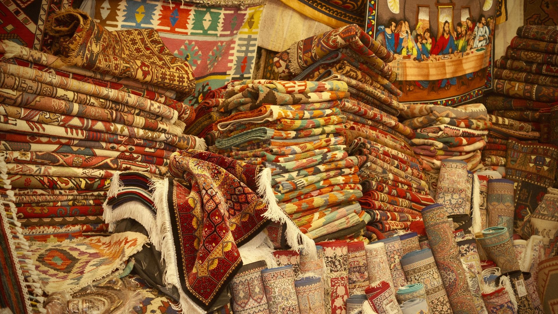 Stacks of colorful carpets and textiles at a market.