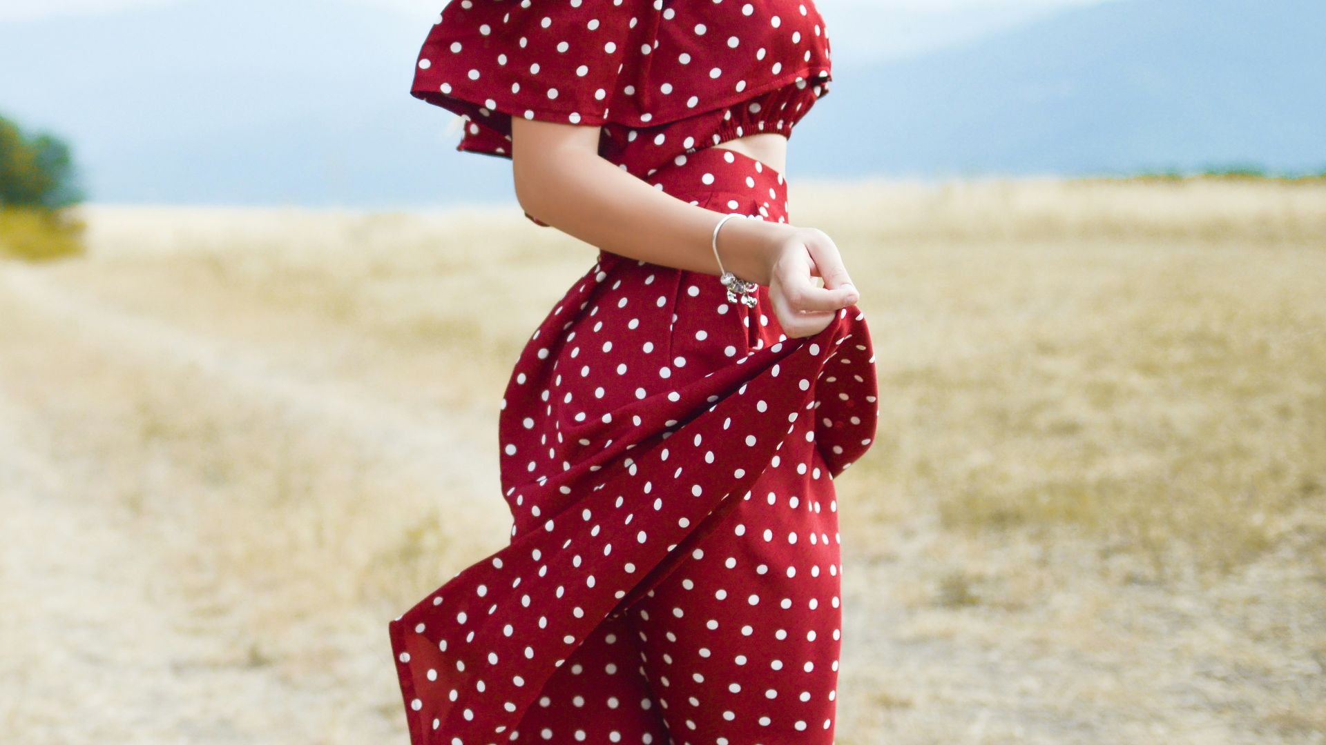 woman in red polka-dot dress standing in the middle of grass field during daytime