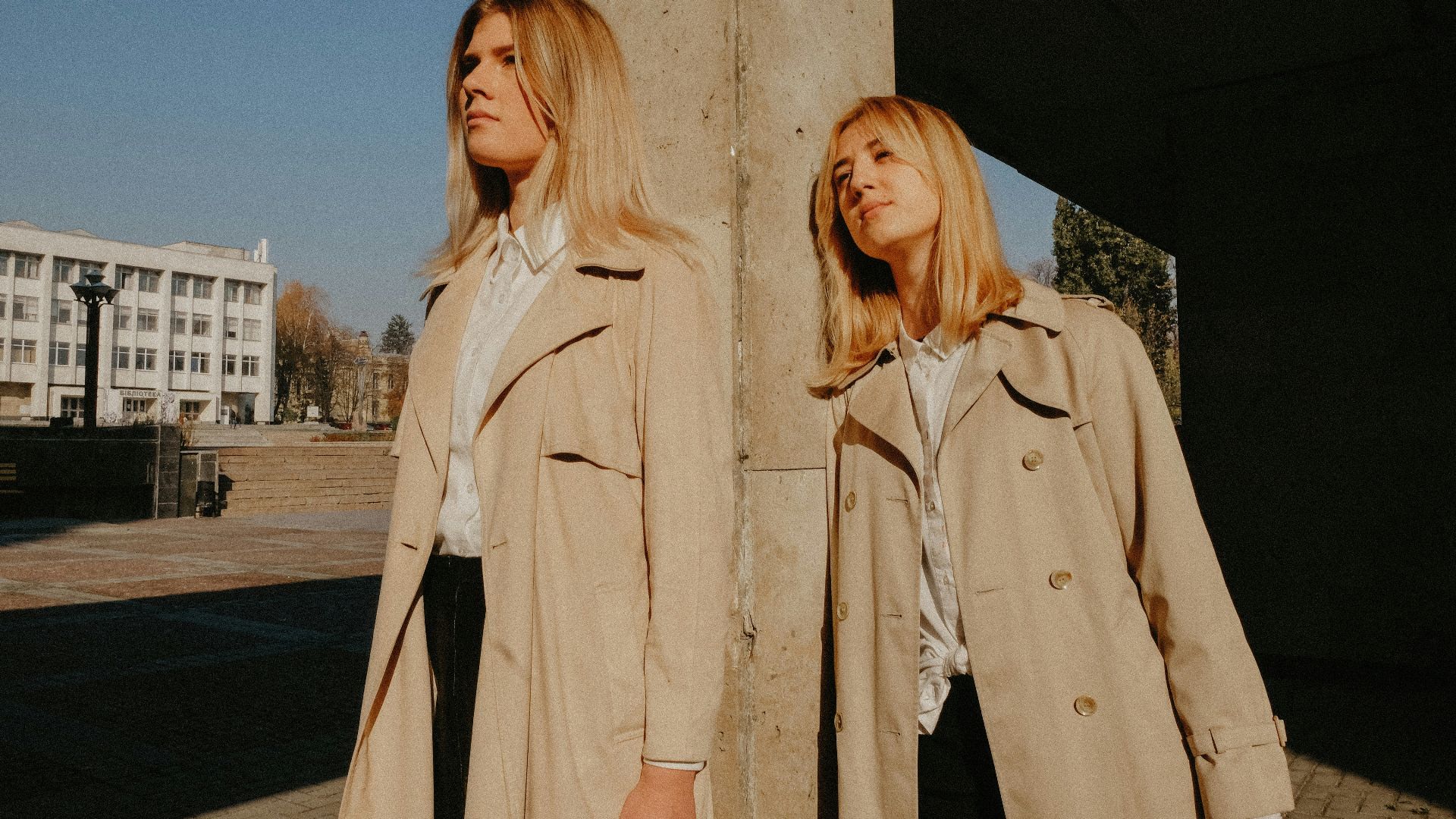 two women wearing brown coat leaning on concrete pillar