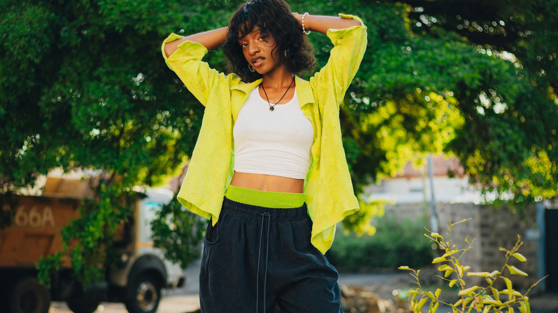 Woman standing outdoors with hands behind head.