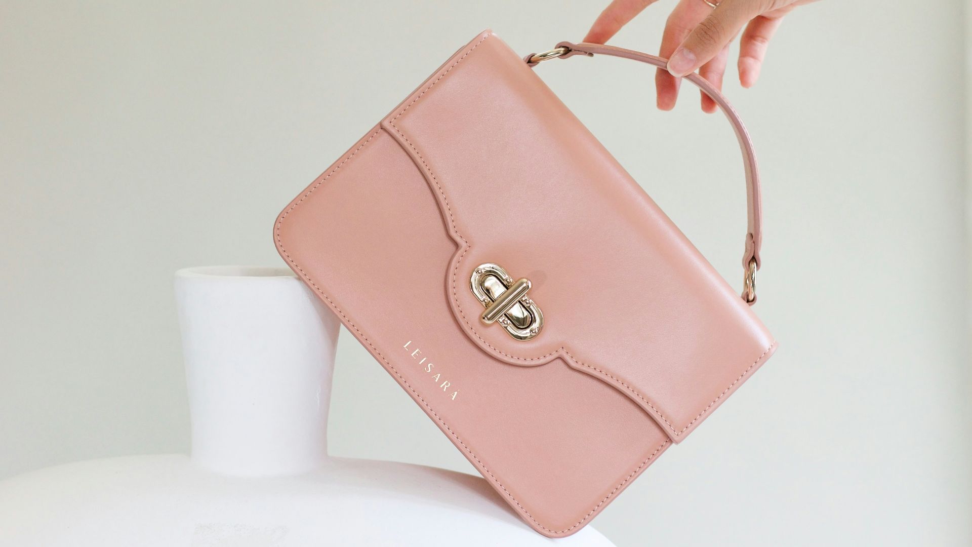 a woman holding a pink purse over a white vase