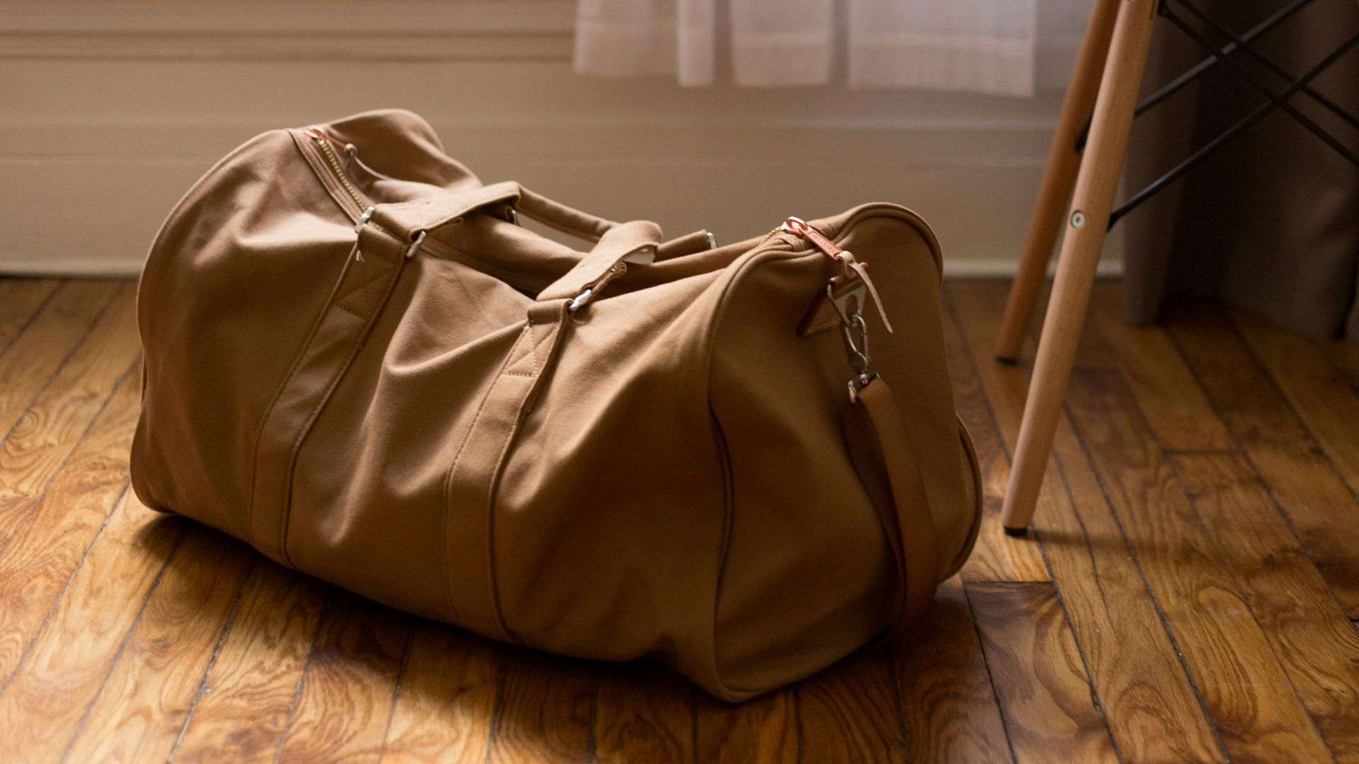 brown duffel bag beside white and brown wooden chair