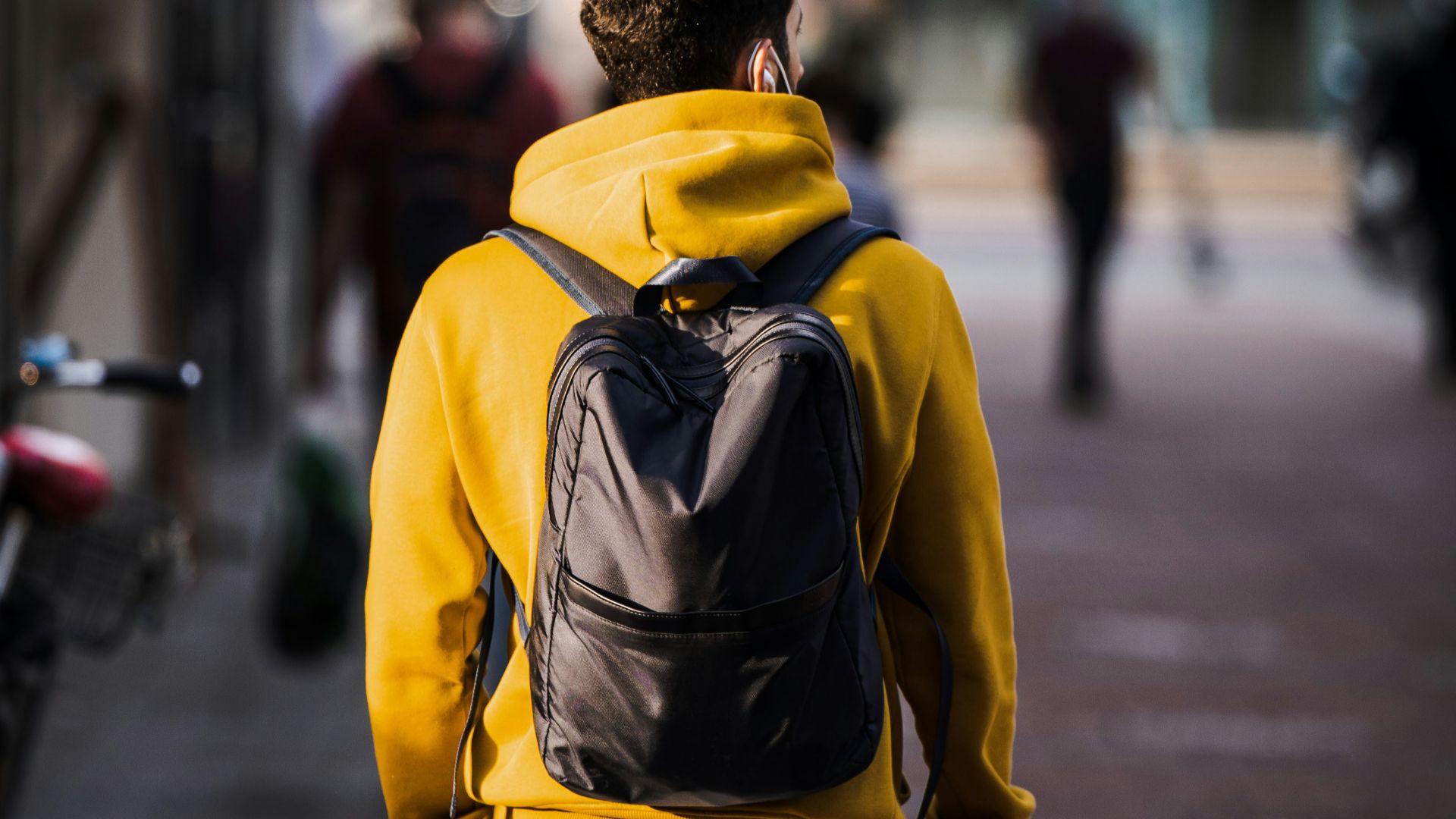 man in yellow and black backpack walking on sidewalk during daytime