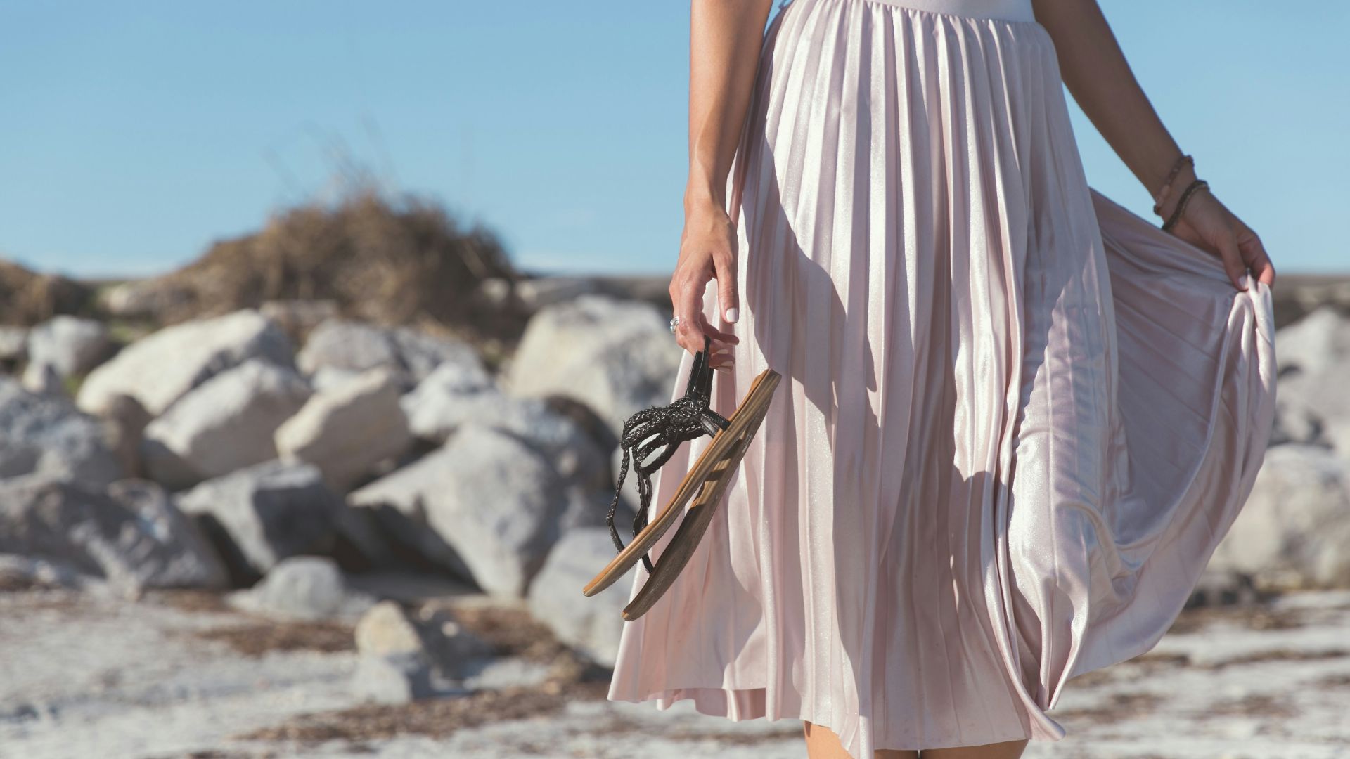 woman wearing white skirt holding black leather flat sandals standing