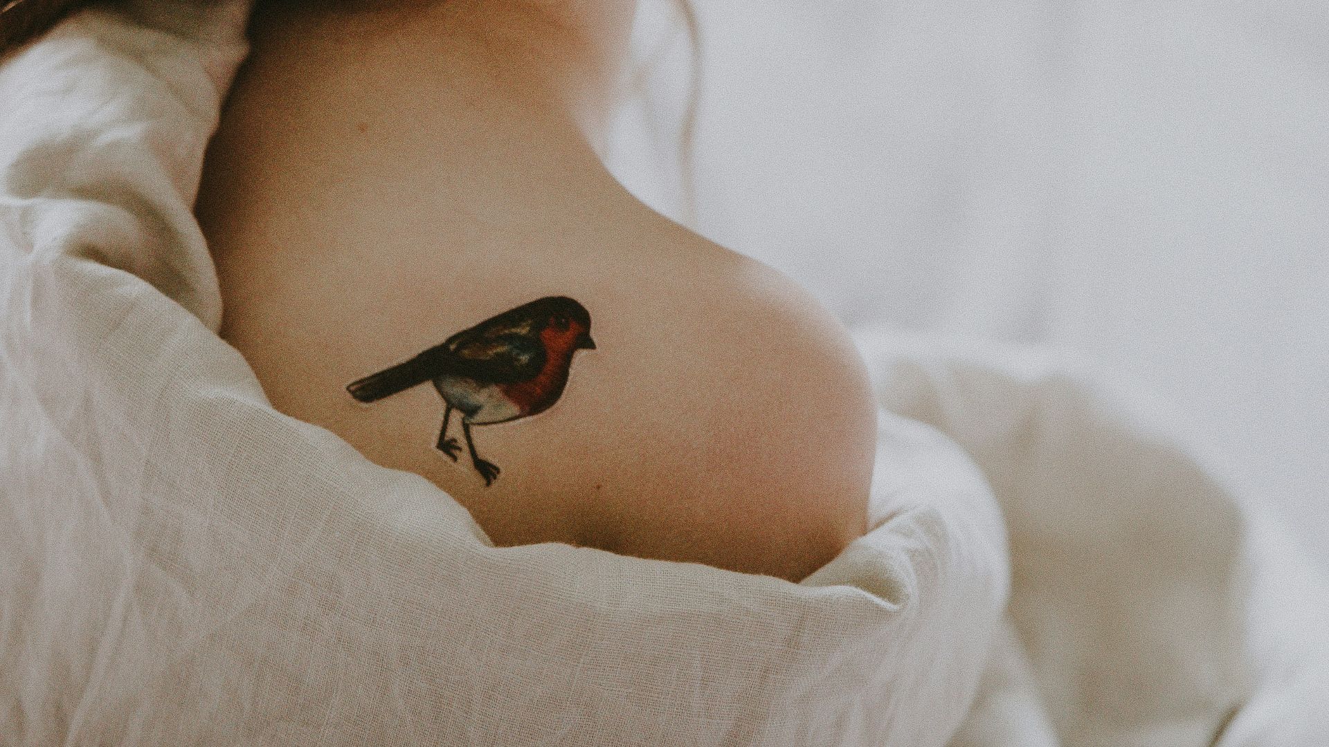 woman with bird tattoo in shoulder laying on white surface