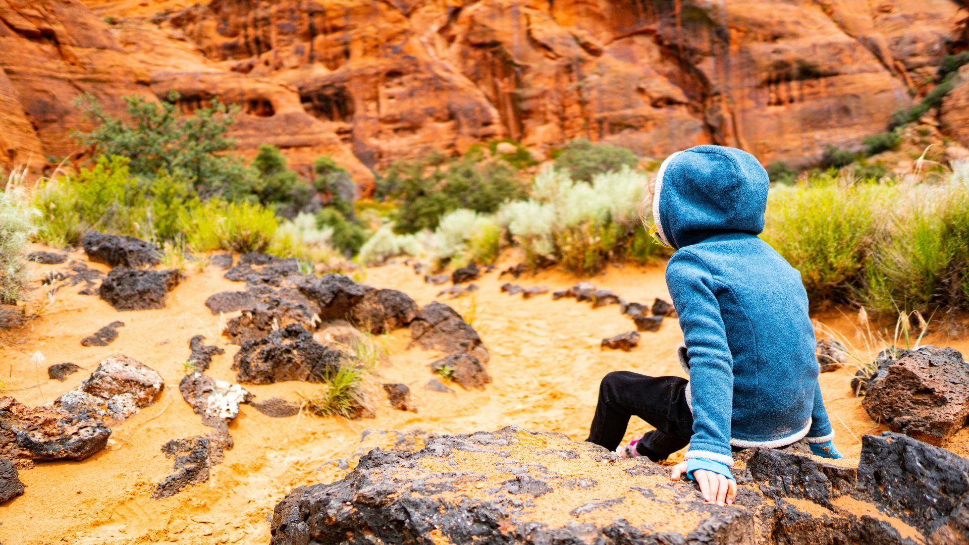 person wearing hoodie sitting on rock facing the rocky mountain