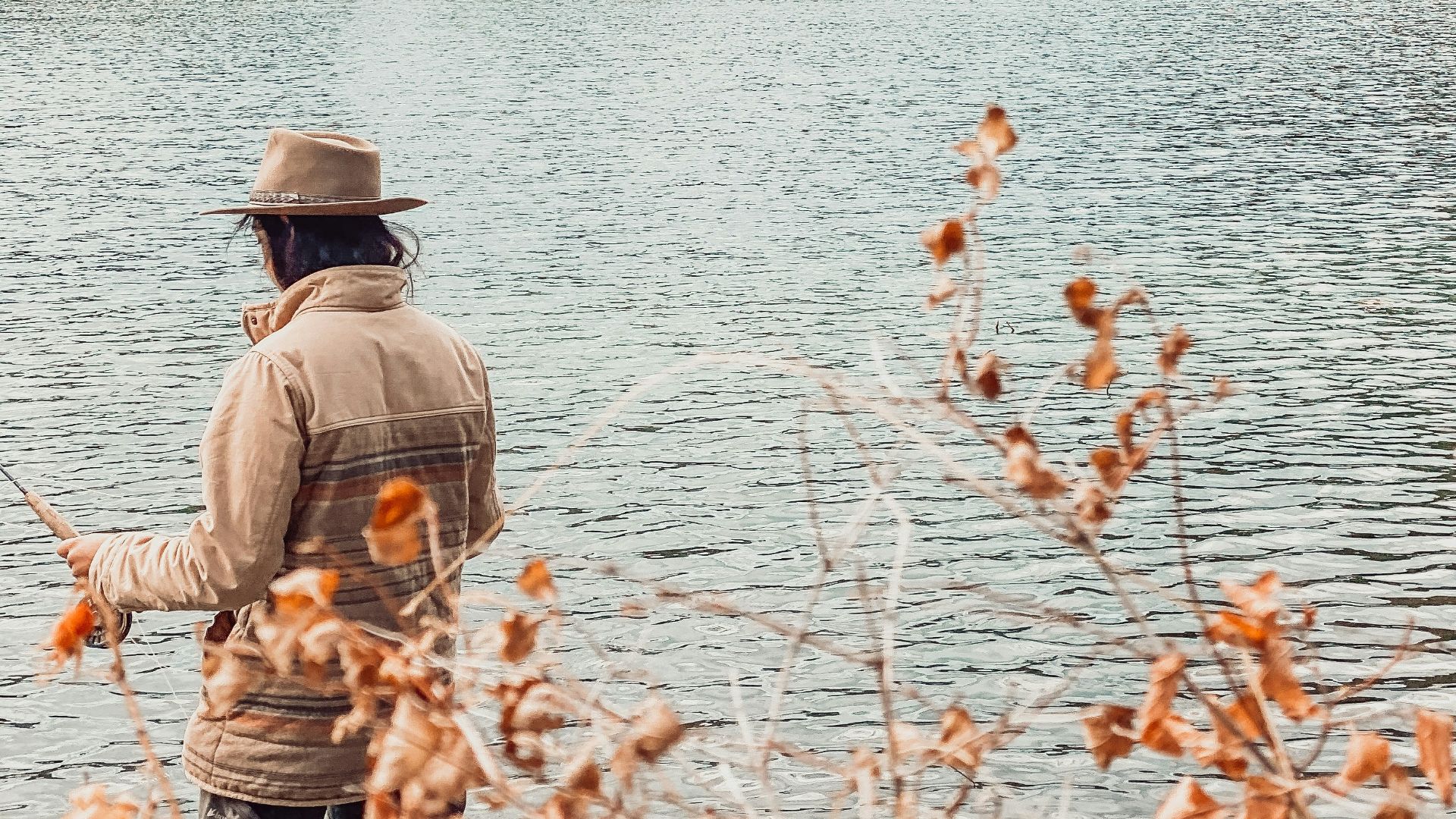 man in brown jacket fishing on lake during daytime