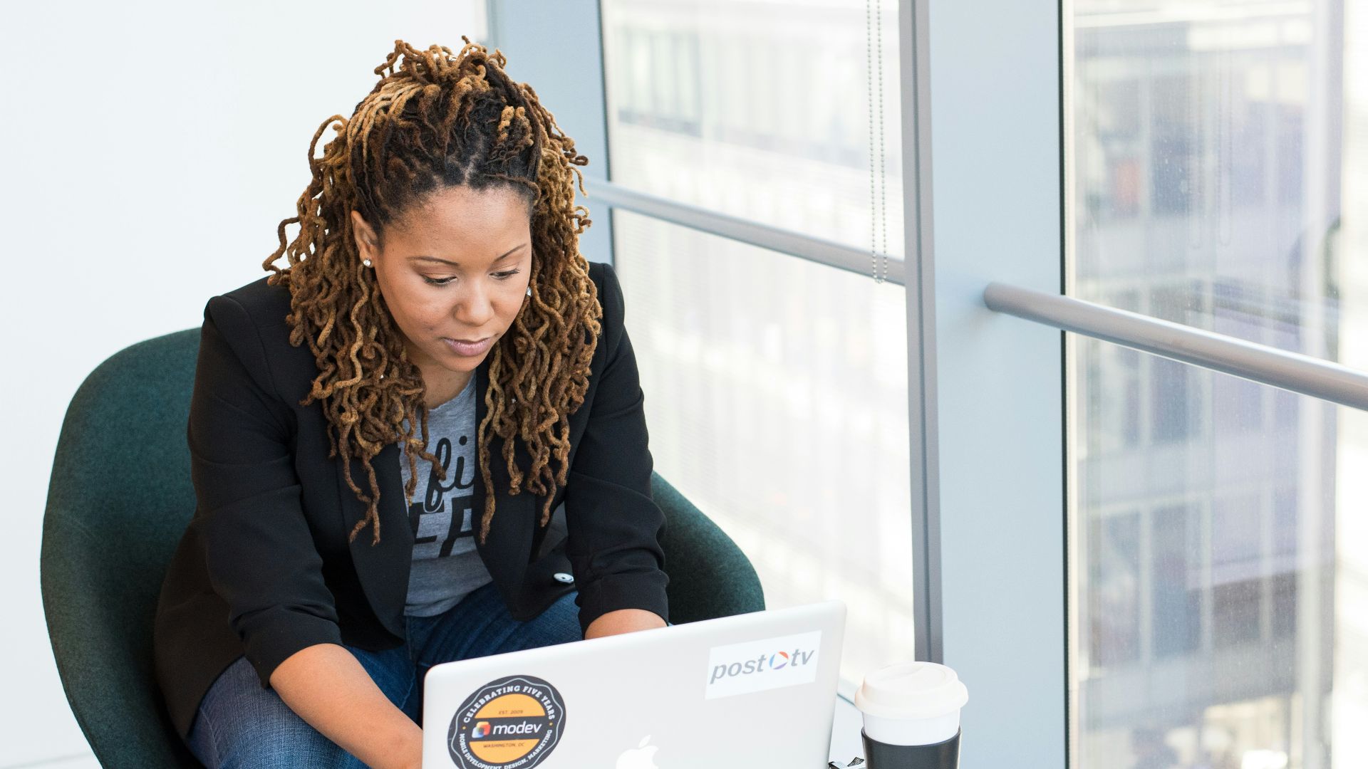 woman sits on padded chair while using MacBook during daytime