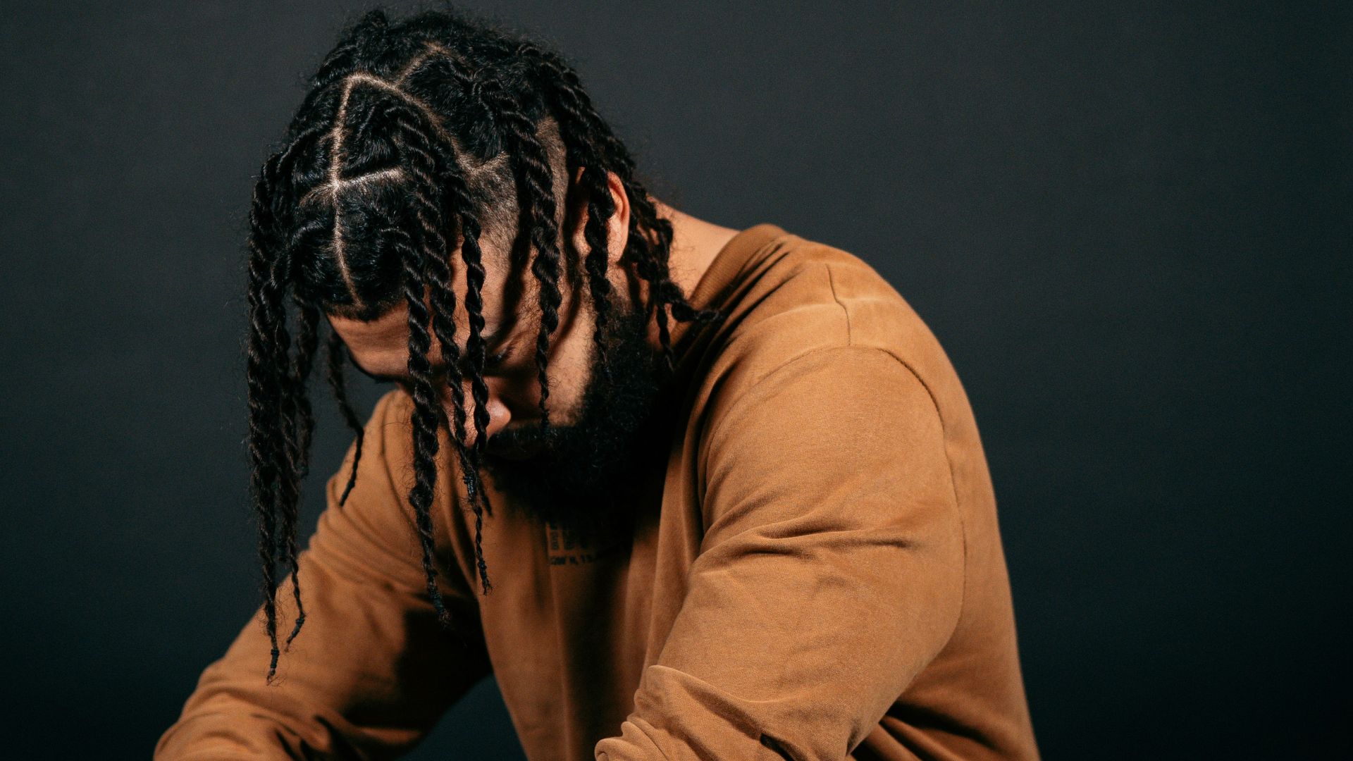 man in brown long sleeve shirt and blue denim jeans sitting on black floor