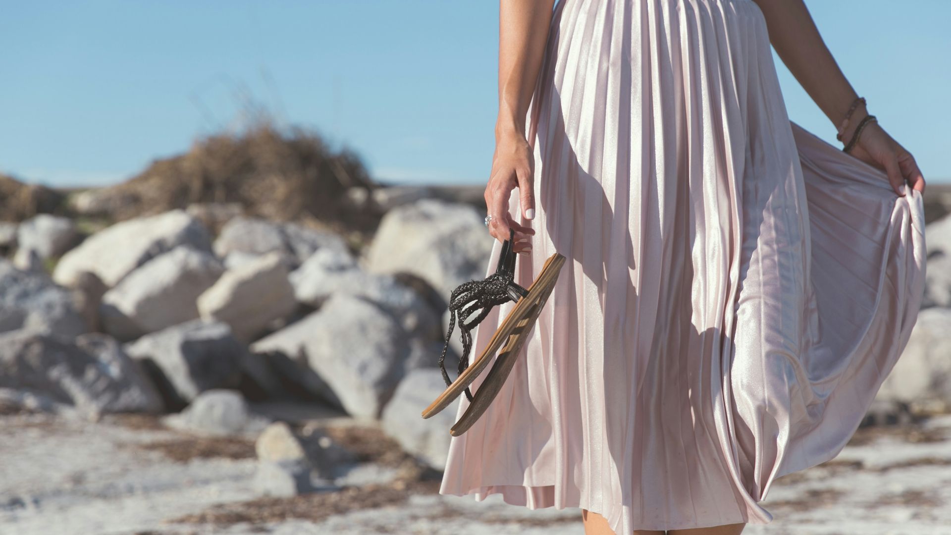 woman wearing white skirt holding black leather flat sandals standing