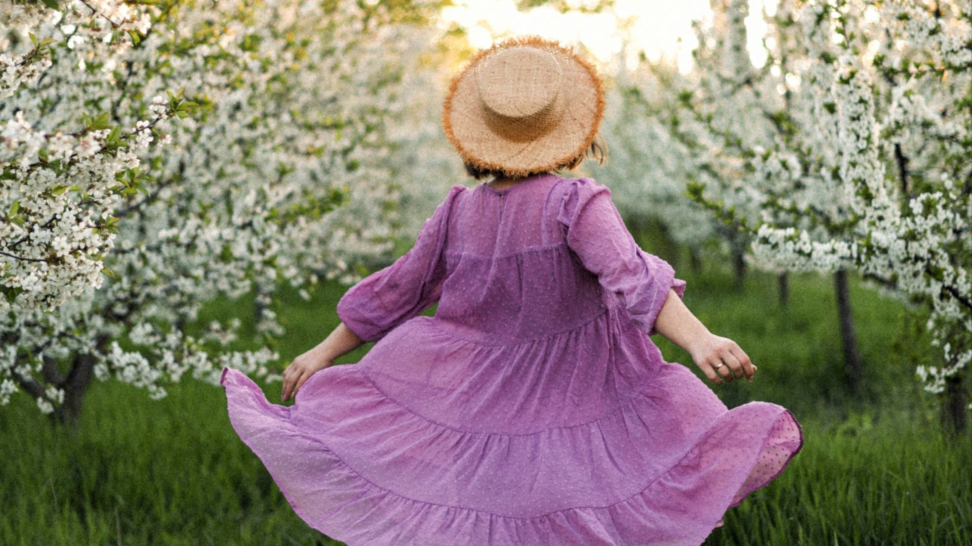 woman in pink dress and brown sun hat sitting on green grass field during daytime