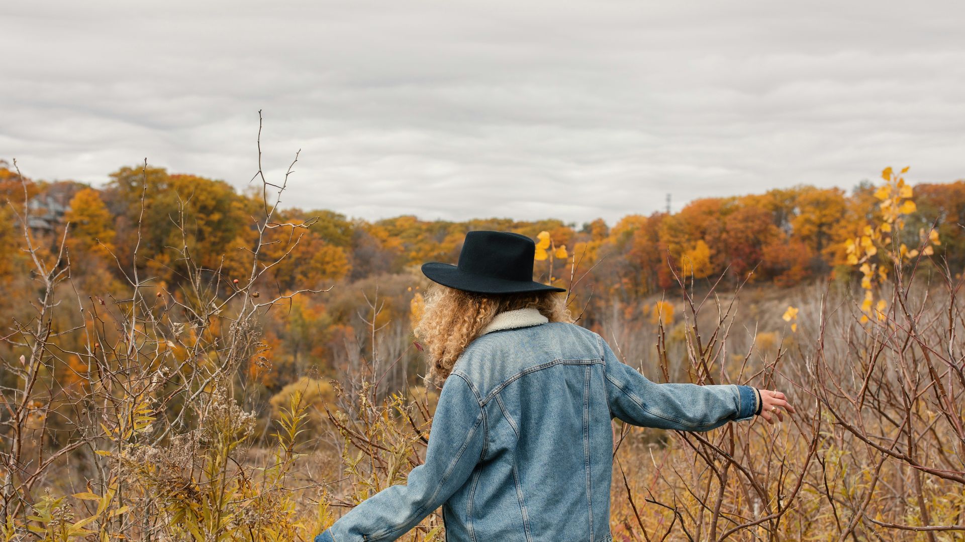 woman wearing blue jacket walking towards the brown grass