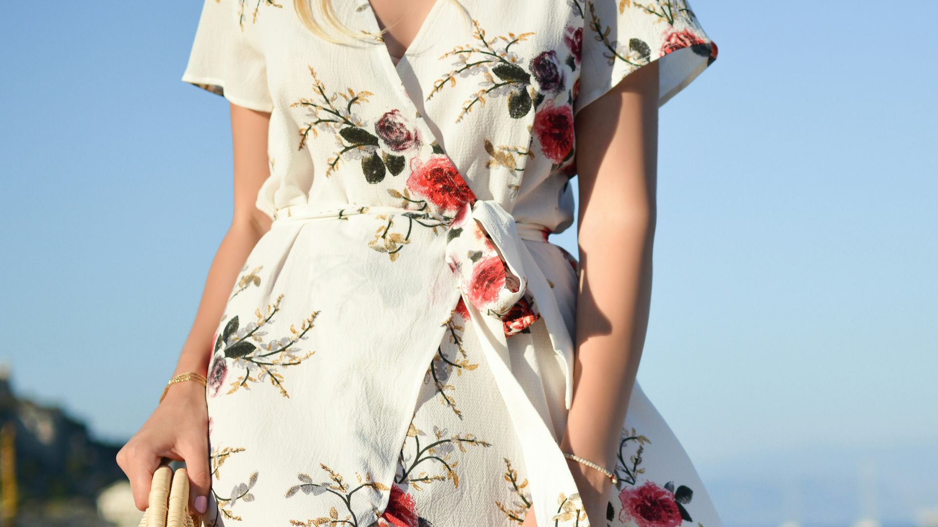woman walking on seaside while holding woven bag