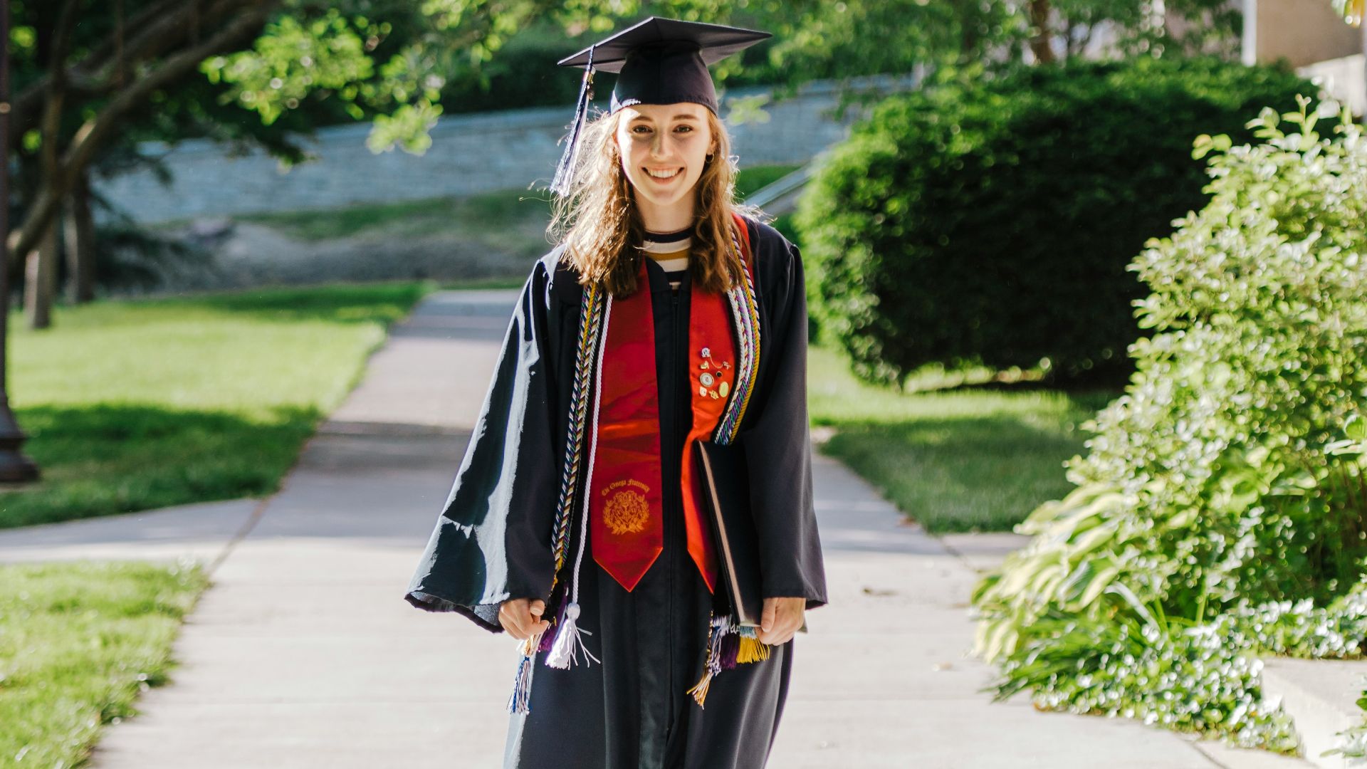 woman in black academic dress and black academic dress standing on gray concrete pathway during daytime