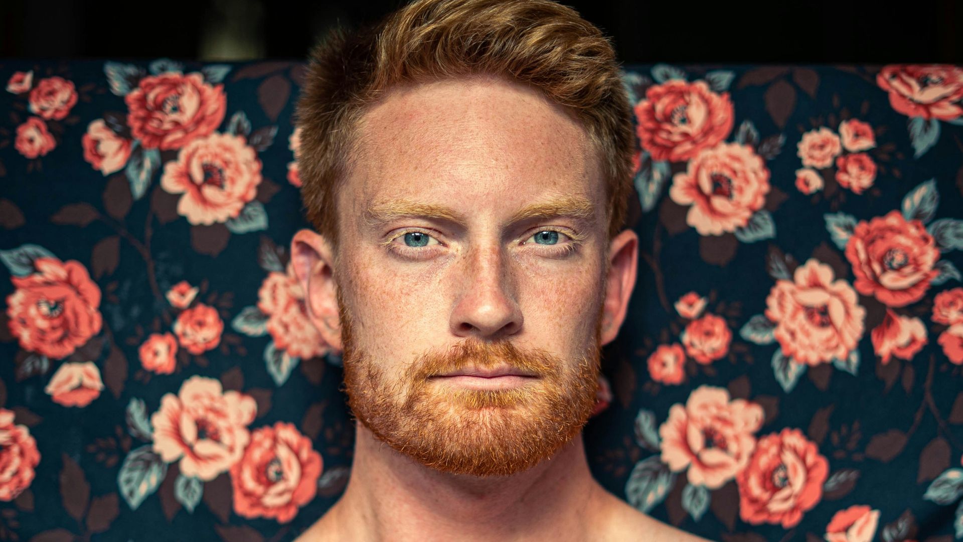 topless man sitting on purple and white floral textile