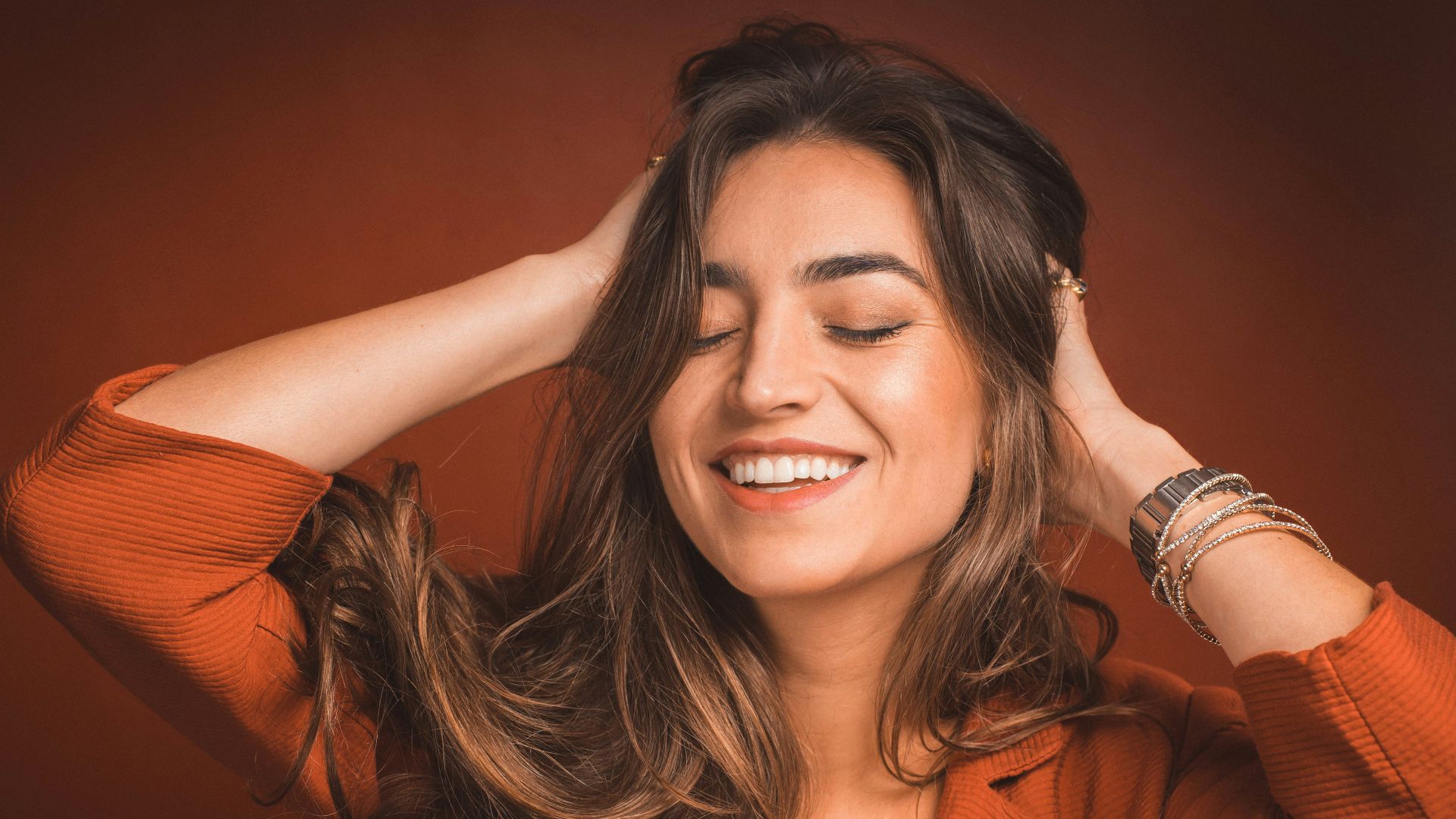 smiling woman in brown top holding hairs