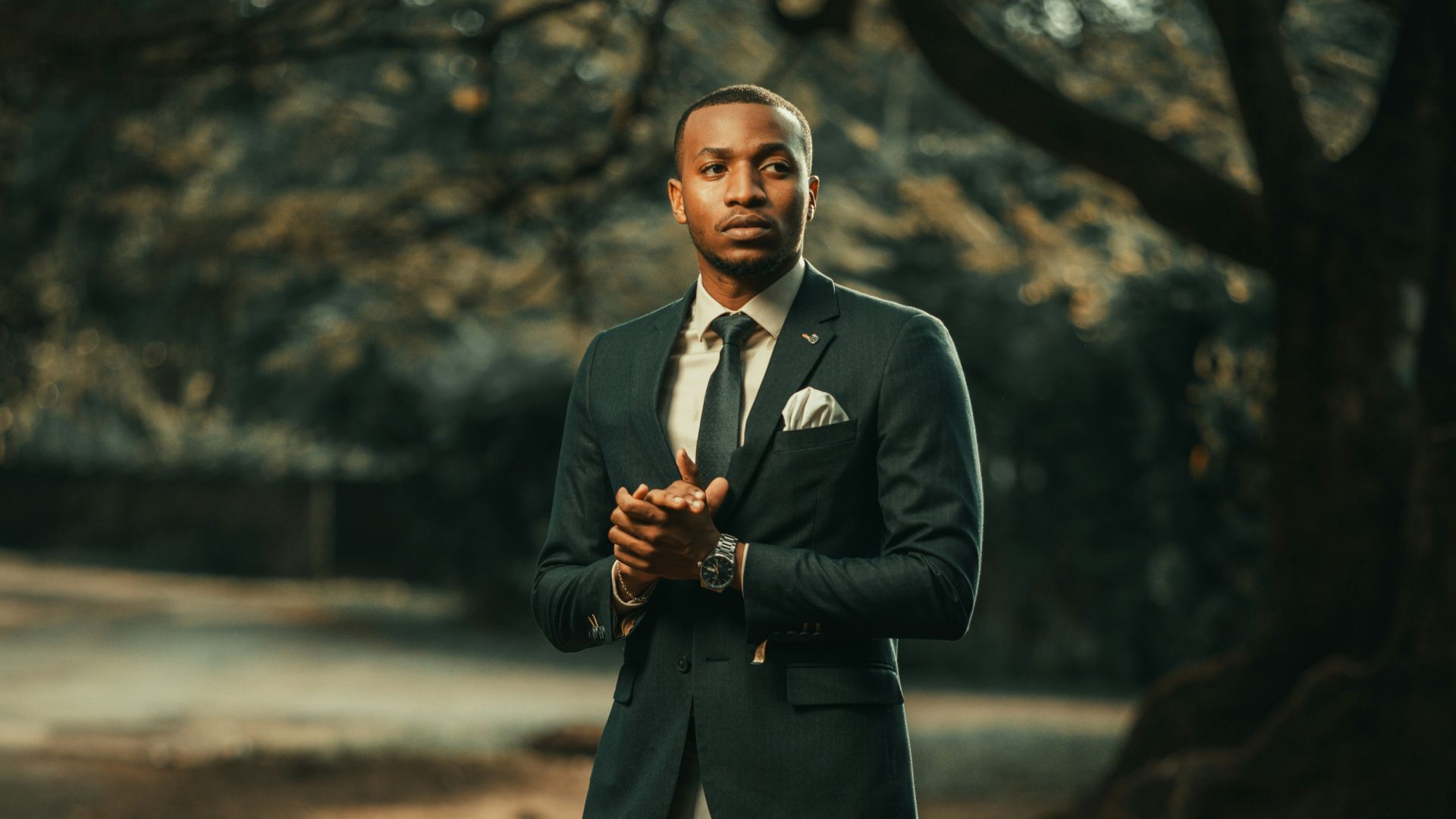 a man in a suit standing in front of a tree