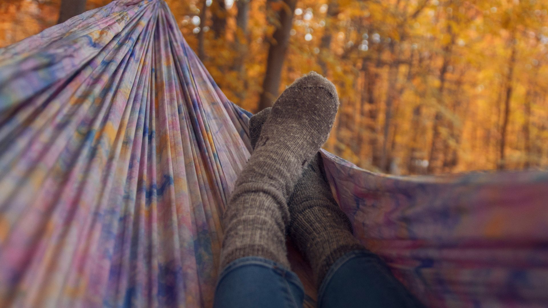 person lying wearing gray socks lying in multicolored hammock