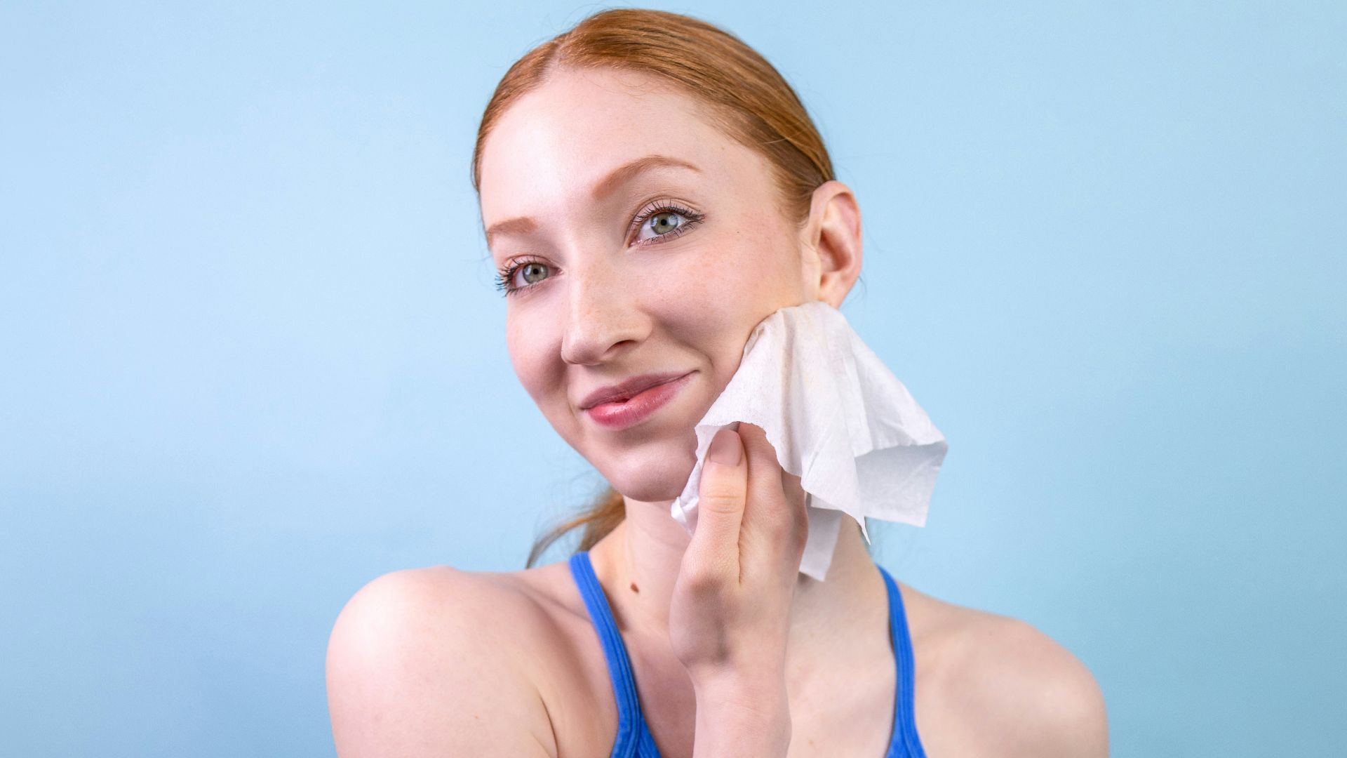 A woman in a blue tank top holding a tissue