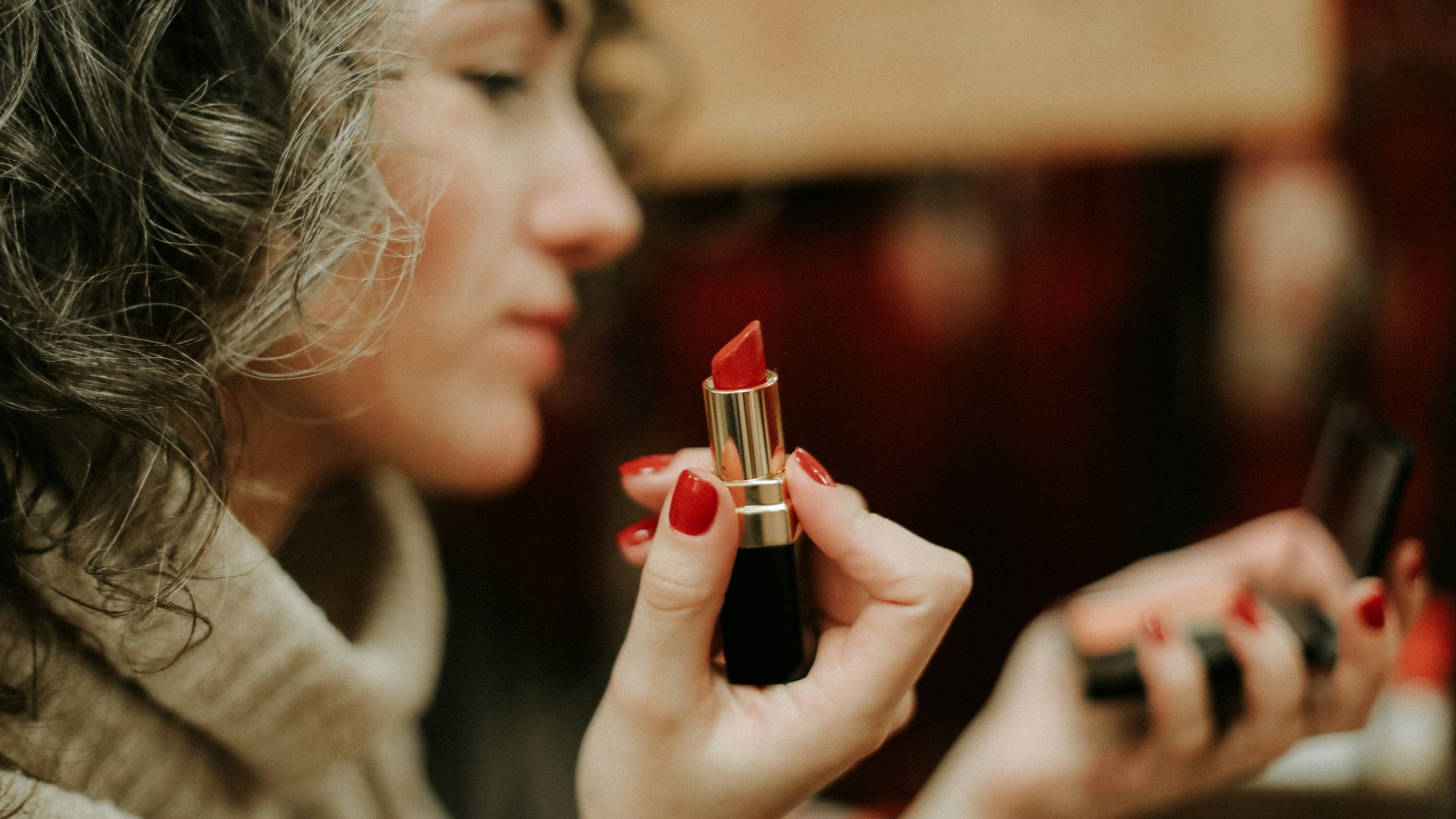 woman in gray sweater holding lipstick