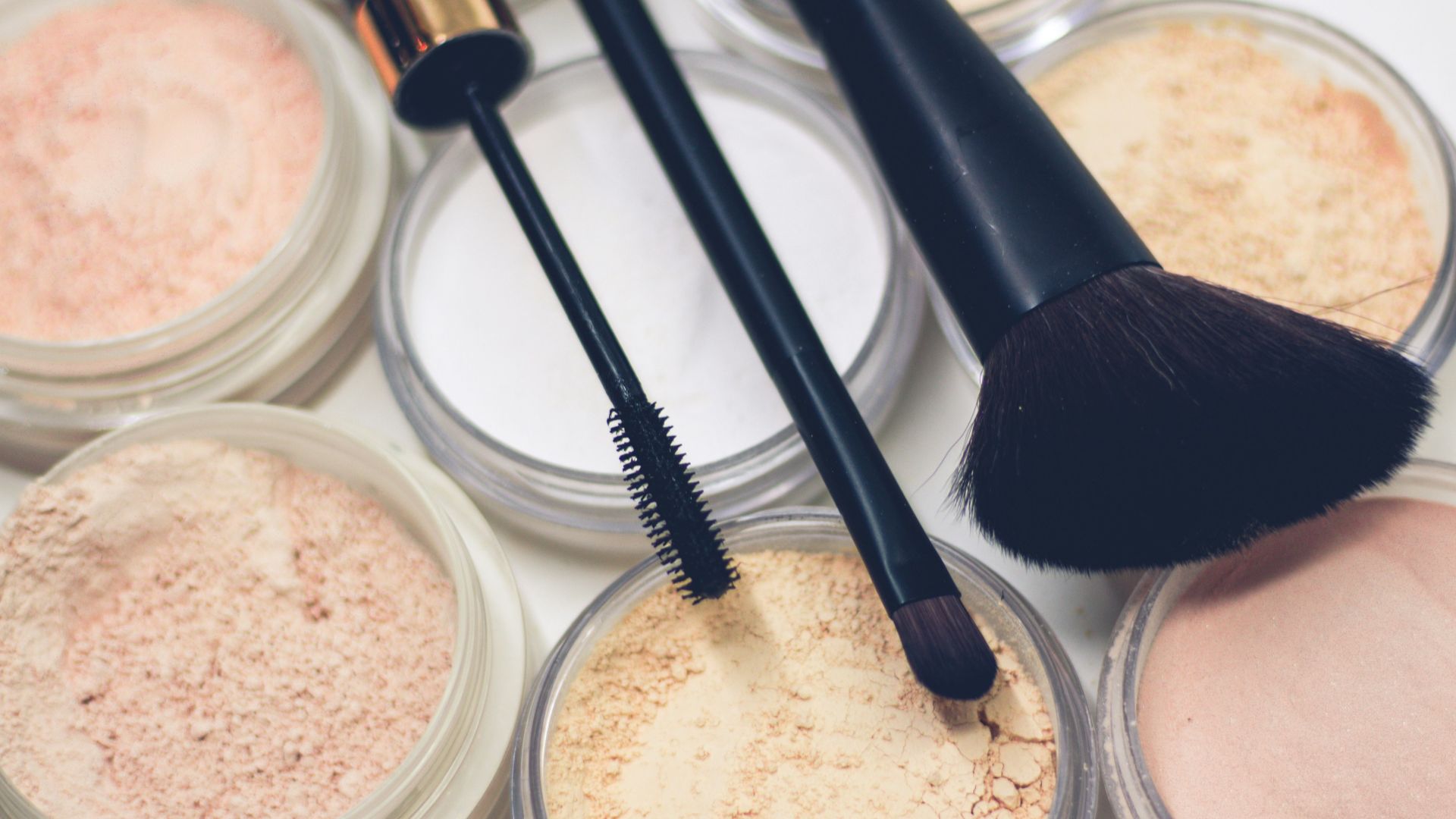 three makeup brushes on top of compact powders