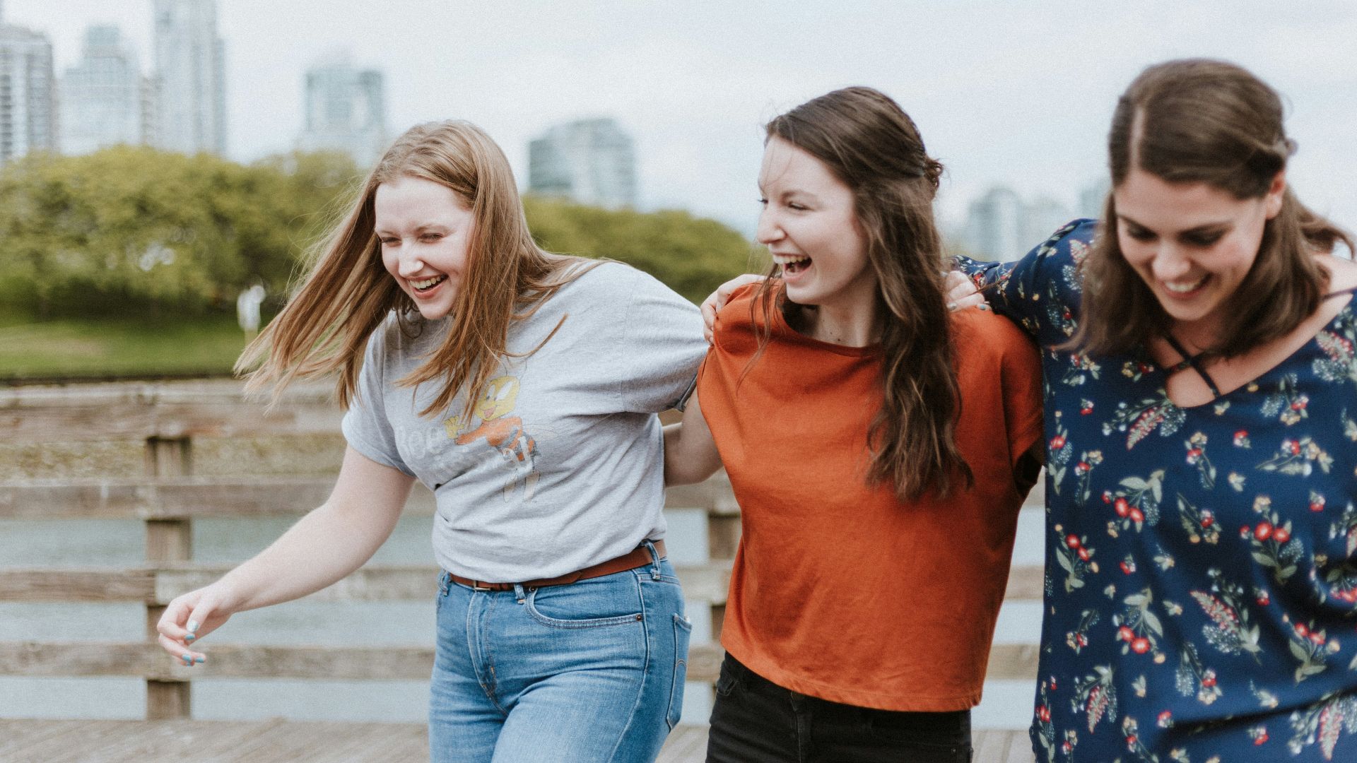 three women walking on brown wooden dock near high rise building during daytime