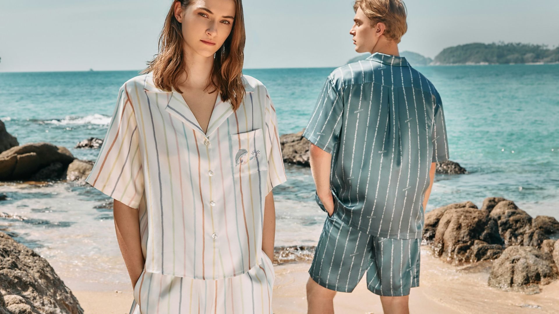 Couple posing in matching striped pajama sets at the beach.