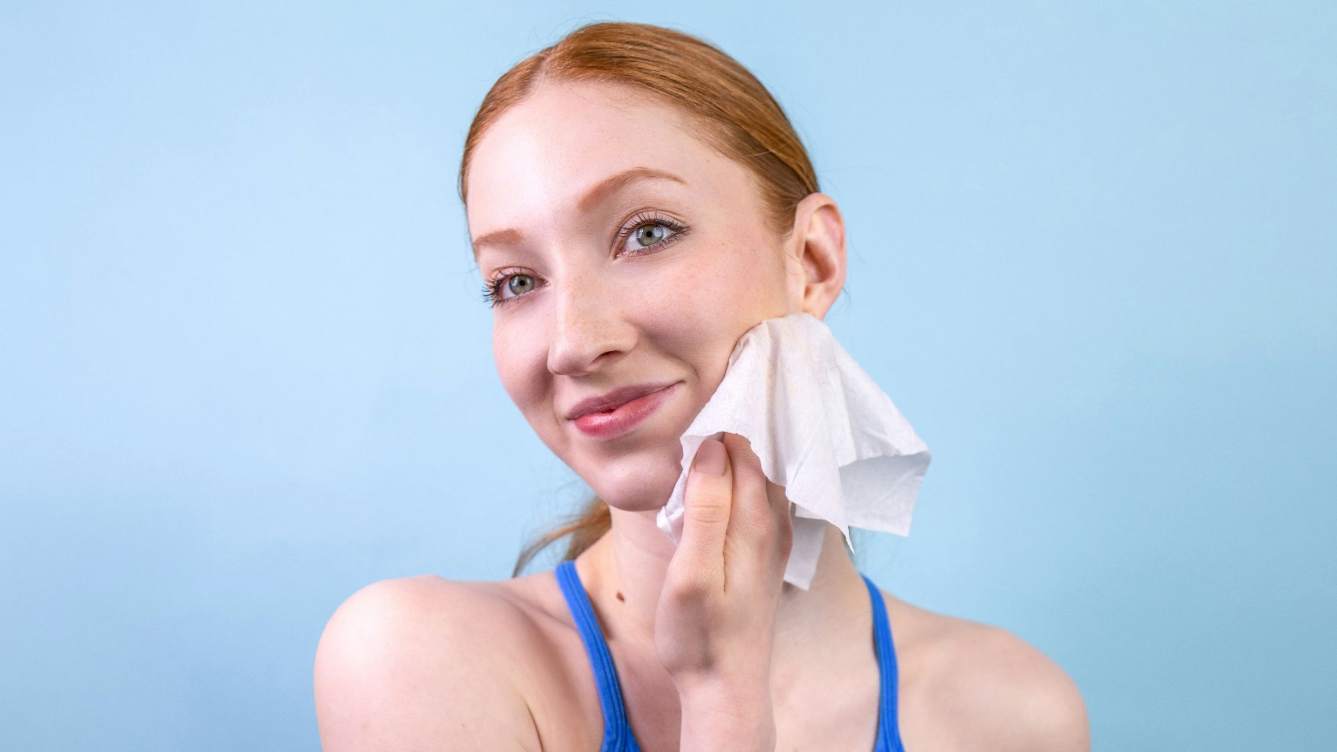 A woman in a blue tank top holding a tissue