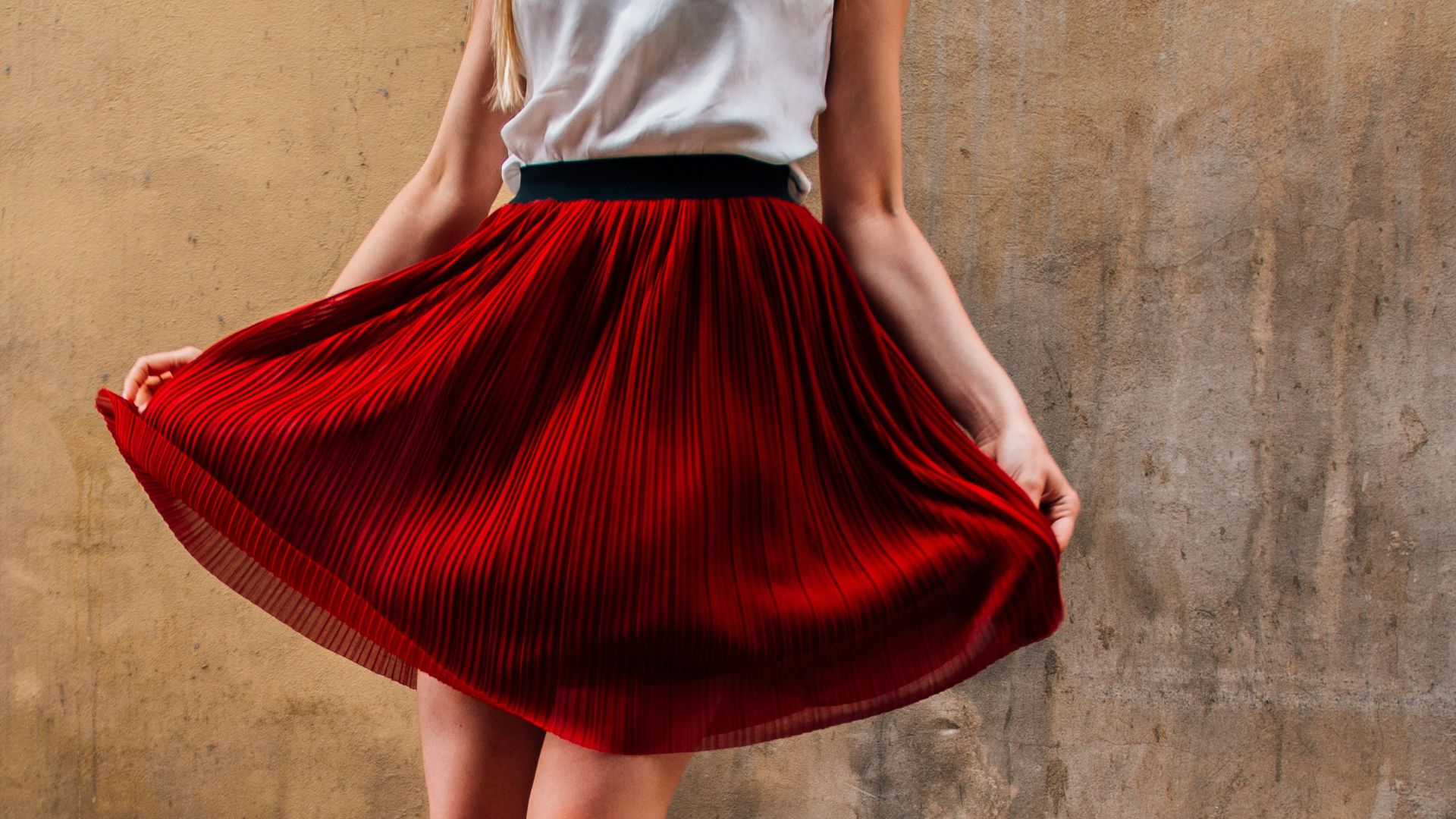 a woman in a red pleated skirt stands on a cobblestone street