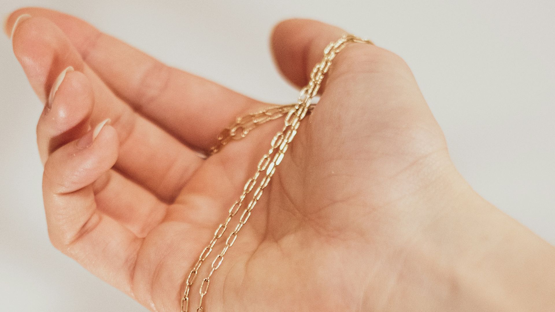 a hand holding a gold heart charm on a chain