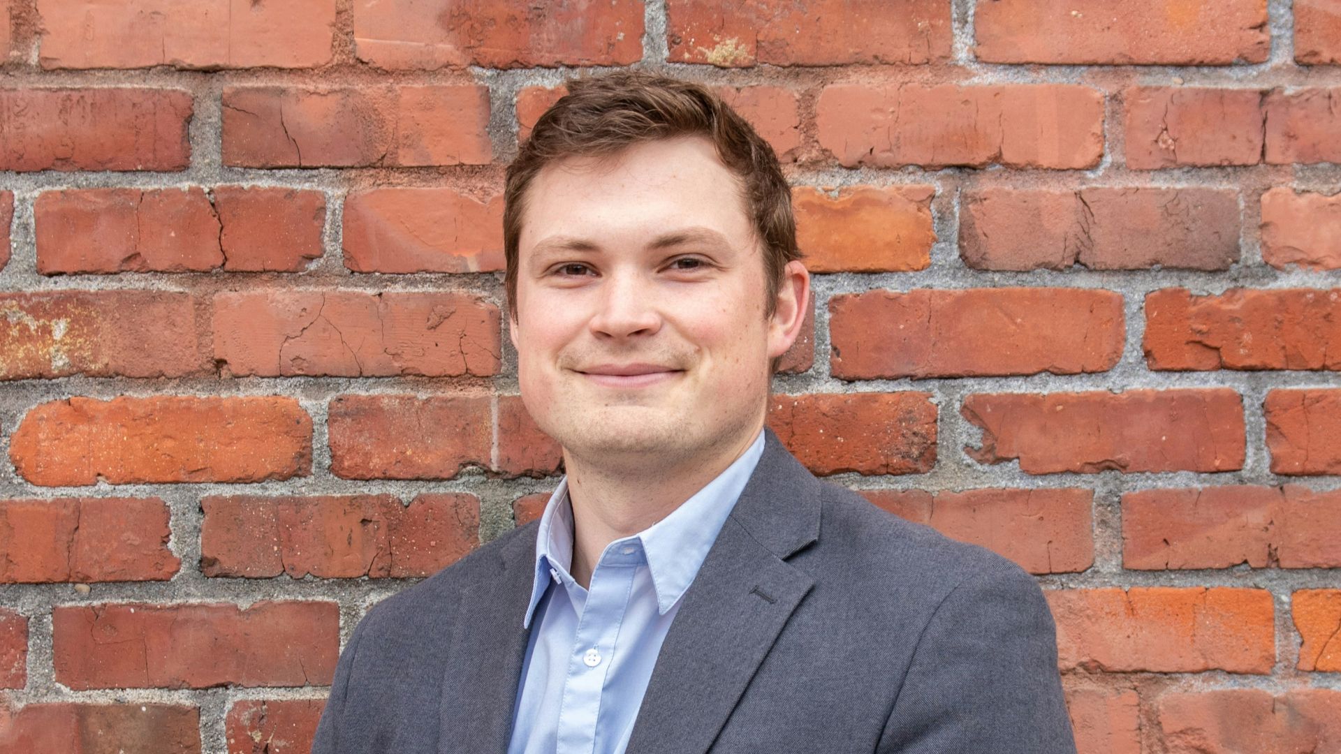 man in gray suit jacket standing beside brown brick wall