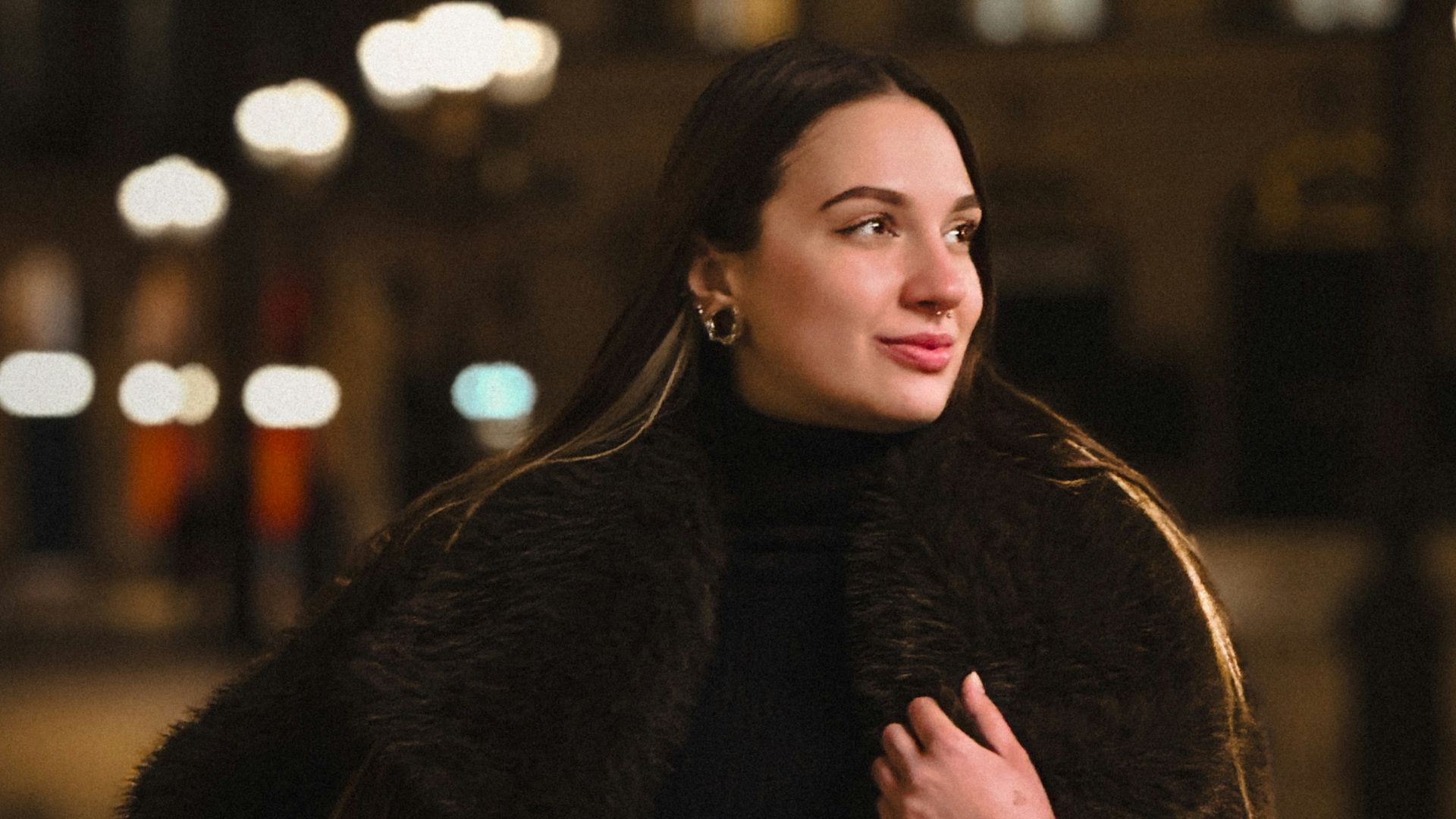 Woman in a fur coat poses at night.