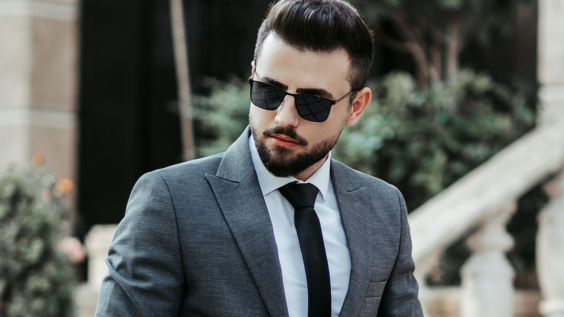 man in gray suit jacket and black pants wearing black sunglasses standing on gray concrete stairs