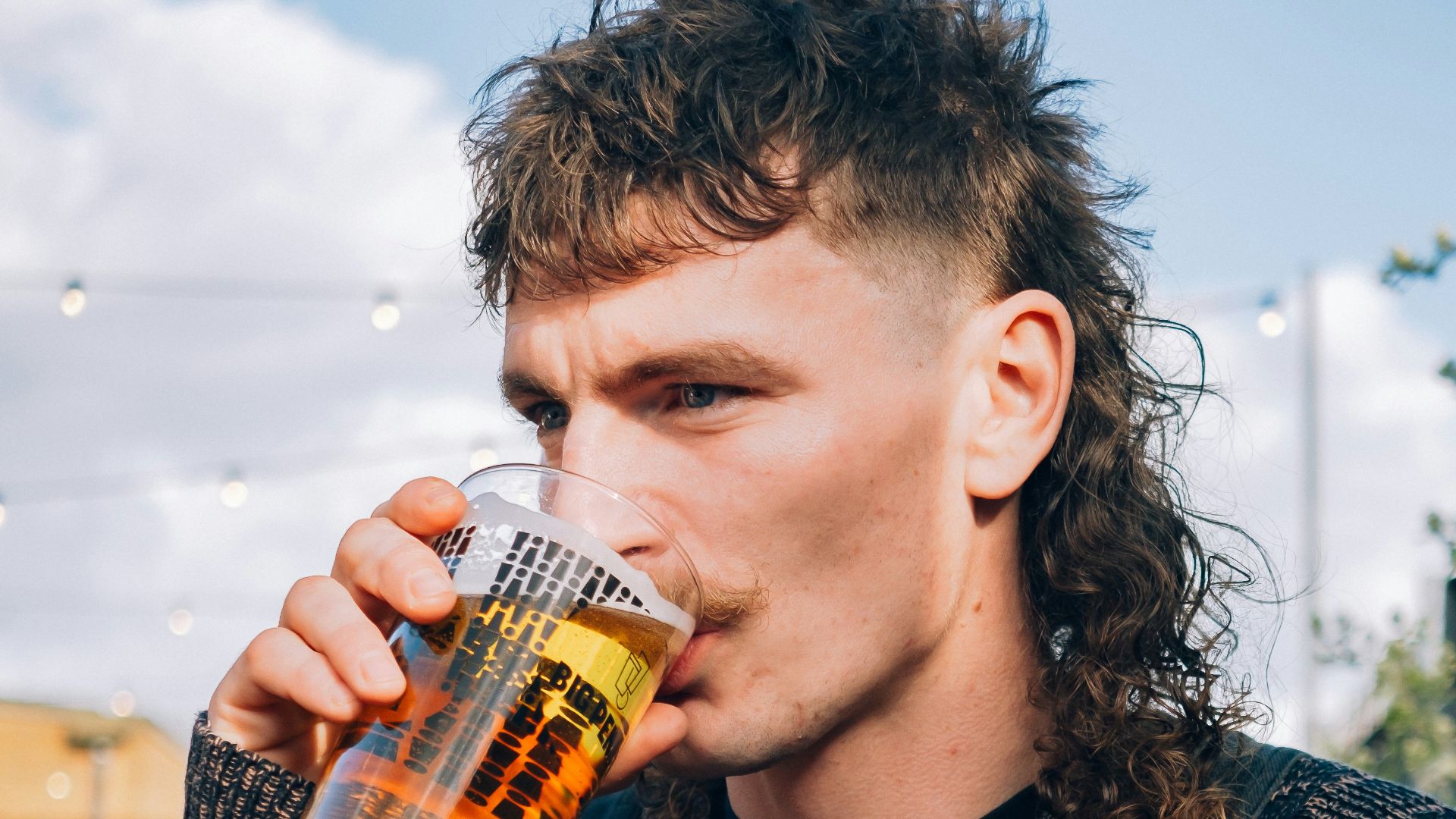 a man with long hair drinking a beer