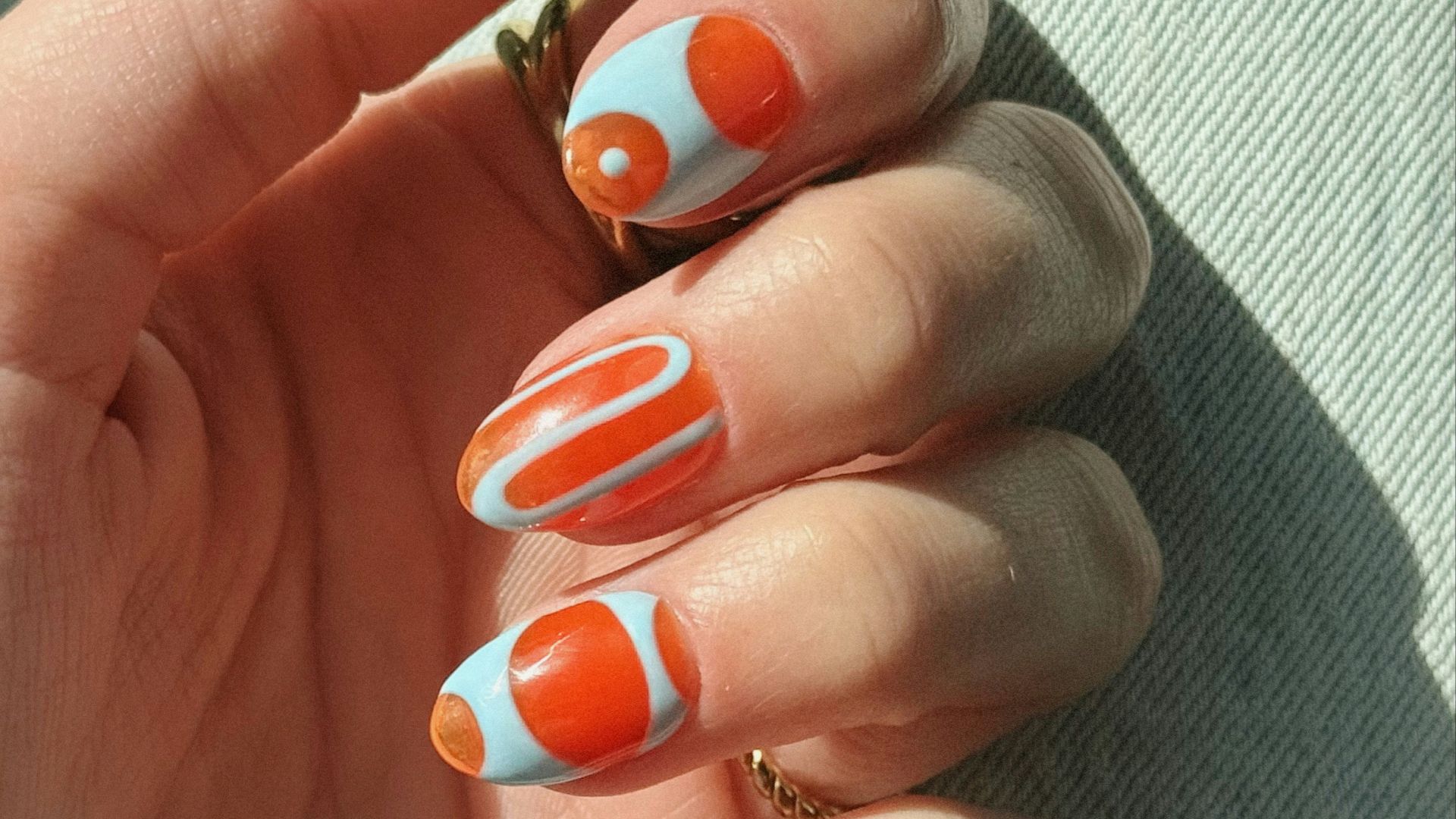 Hand with light blue and orange abstract patterned nails