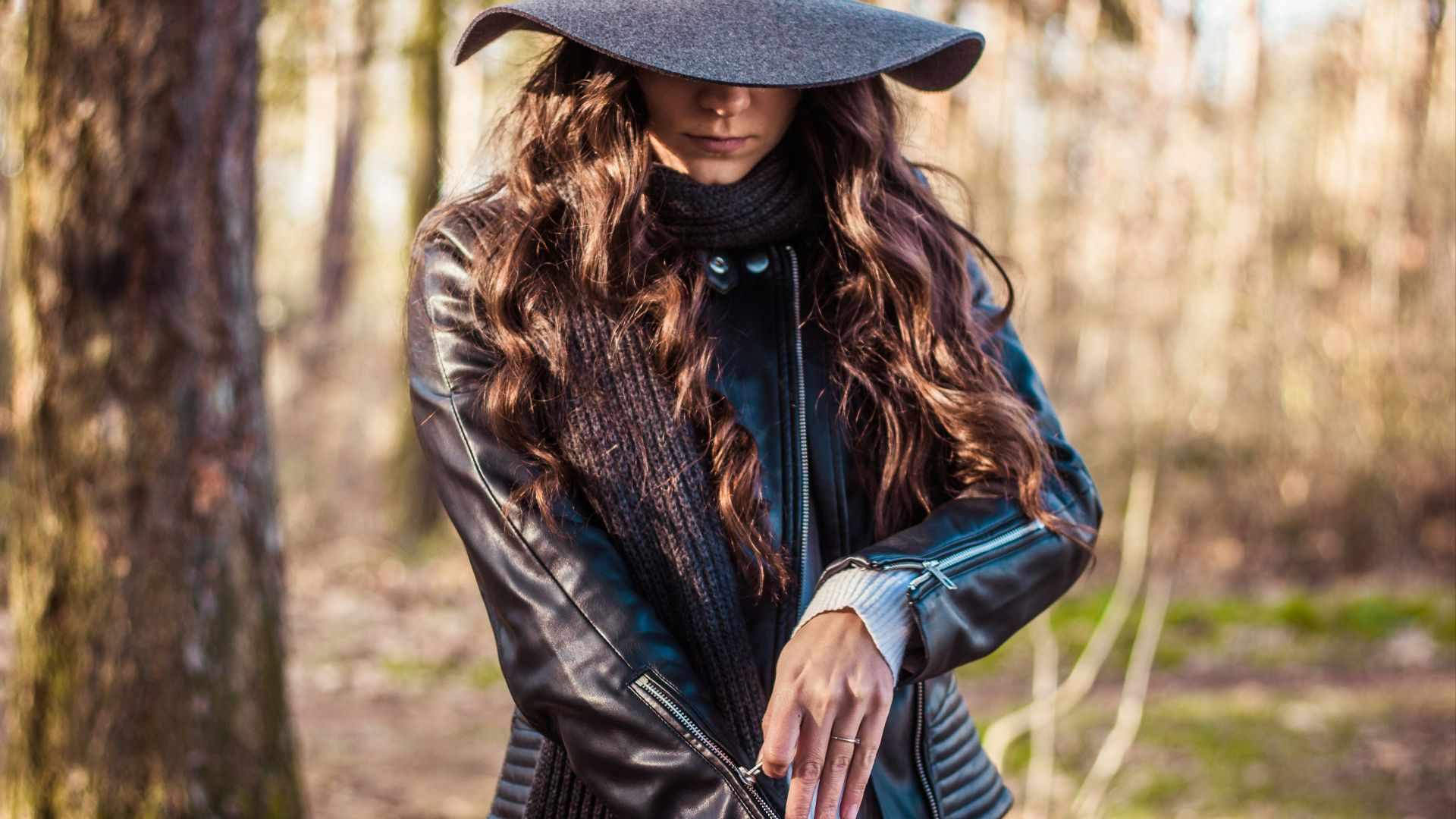 shallow focus photography of woman standing in front of tree while zipping her jacket