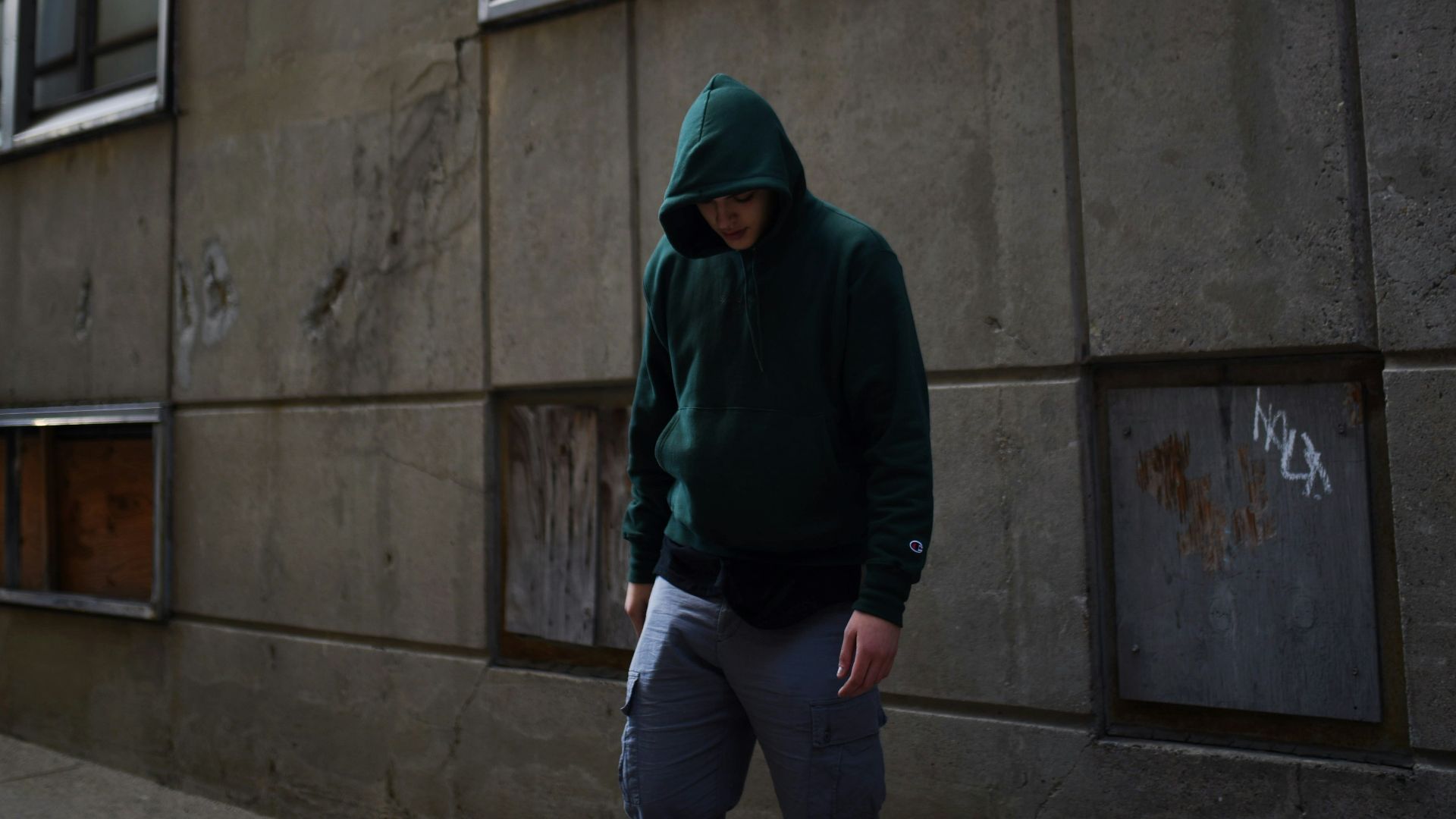 a man in a green hoodie walking down a sidewalk