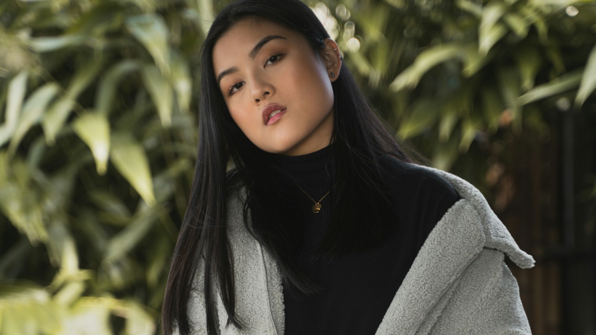 woman in gray coat standing near green tree during daytime