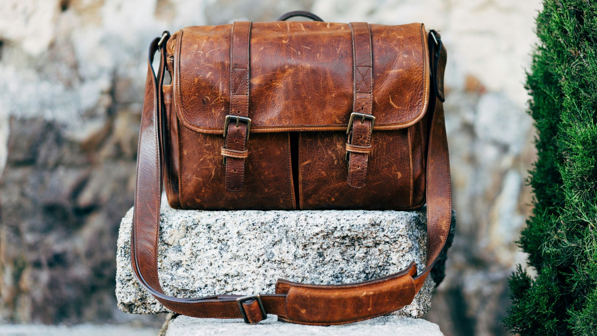brown leather satchel bag on gray concrete surface near green plant at daytime