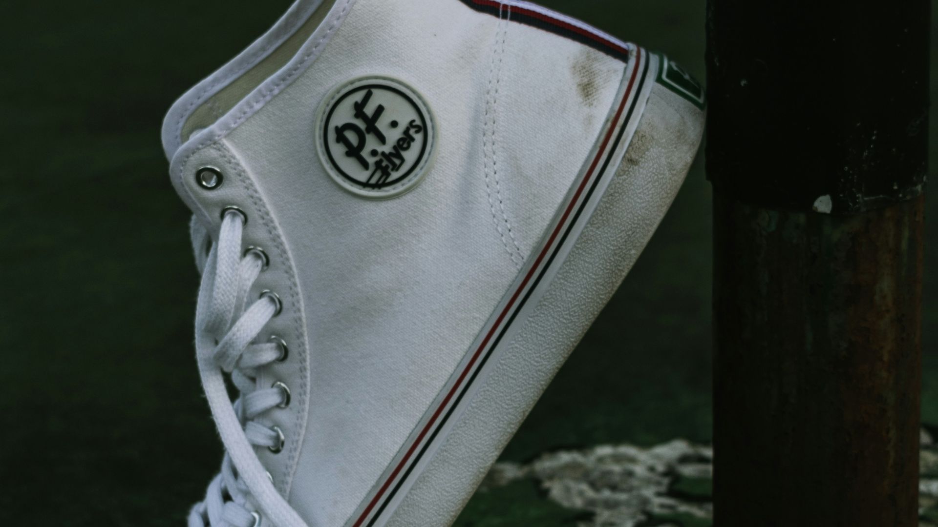 unpaired white PF high-top sneaker leaning on black post
